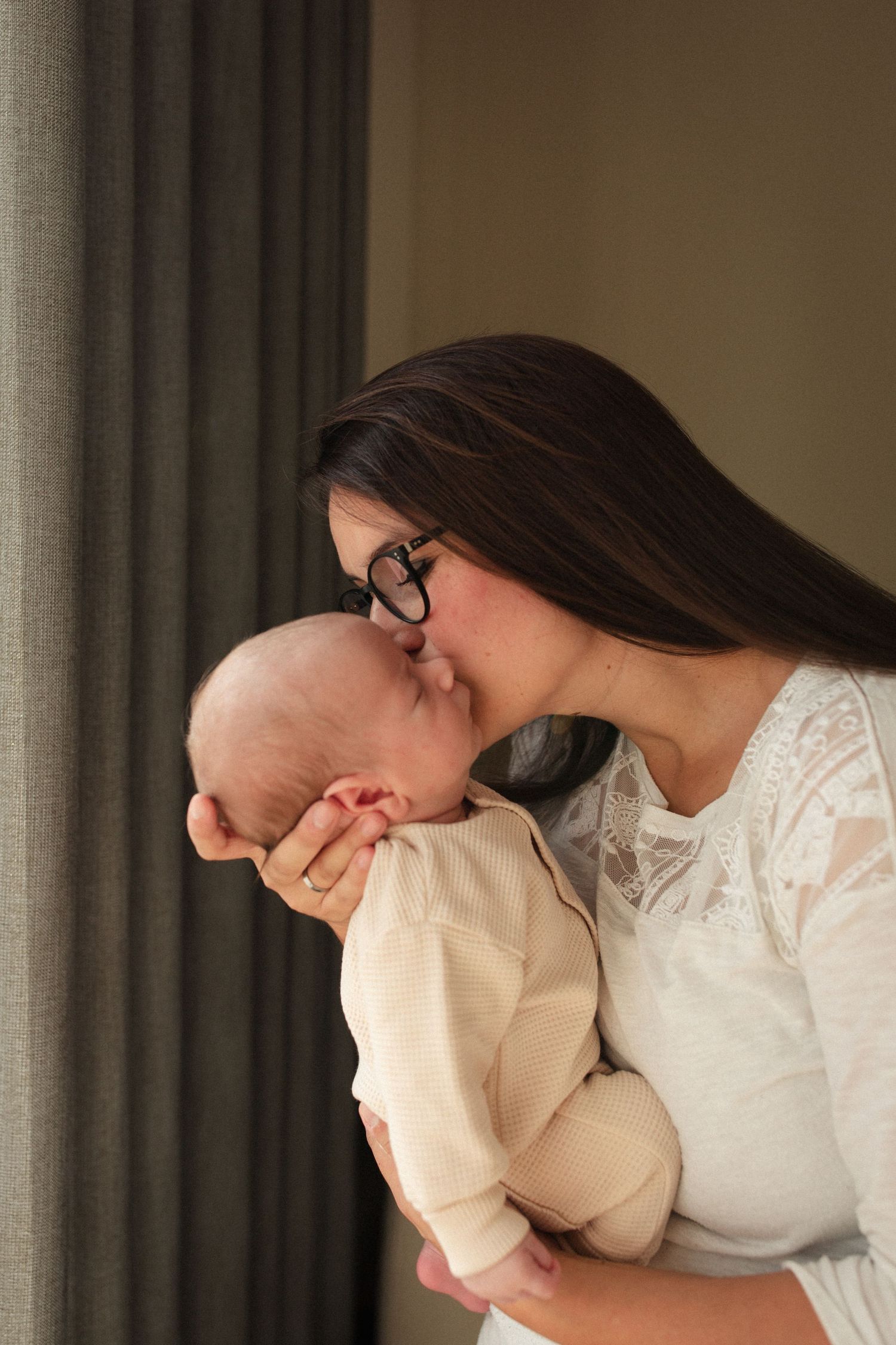 Tender moment between caregiver and infant in cream colored outfit.