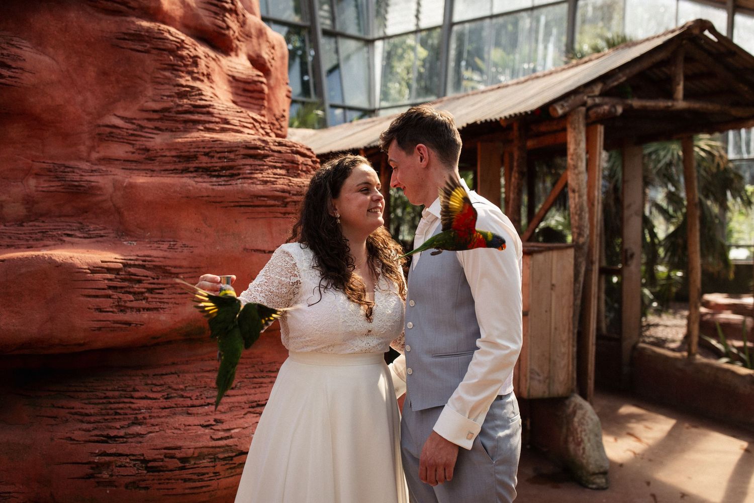 A wedding couple poses together against a rustic red rock wall backdrop in a natural setting.