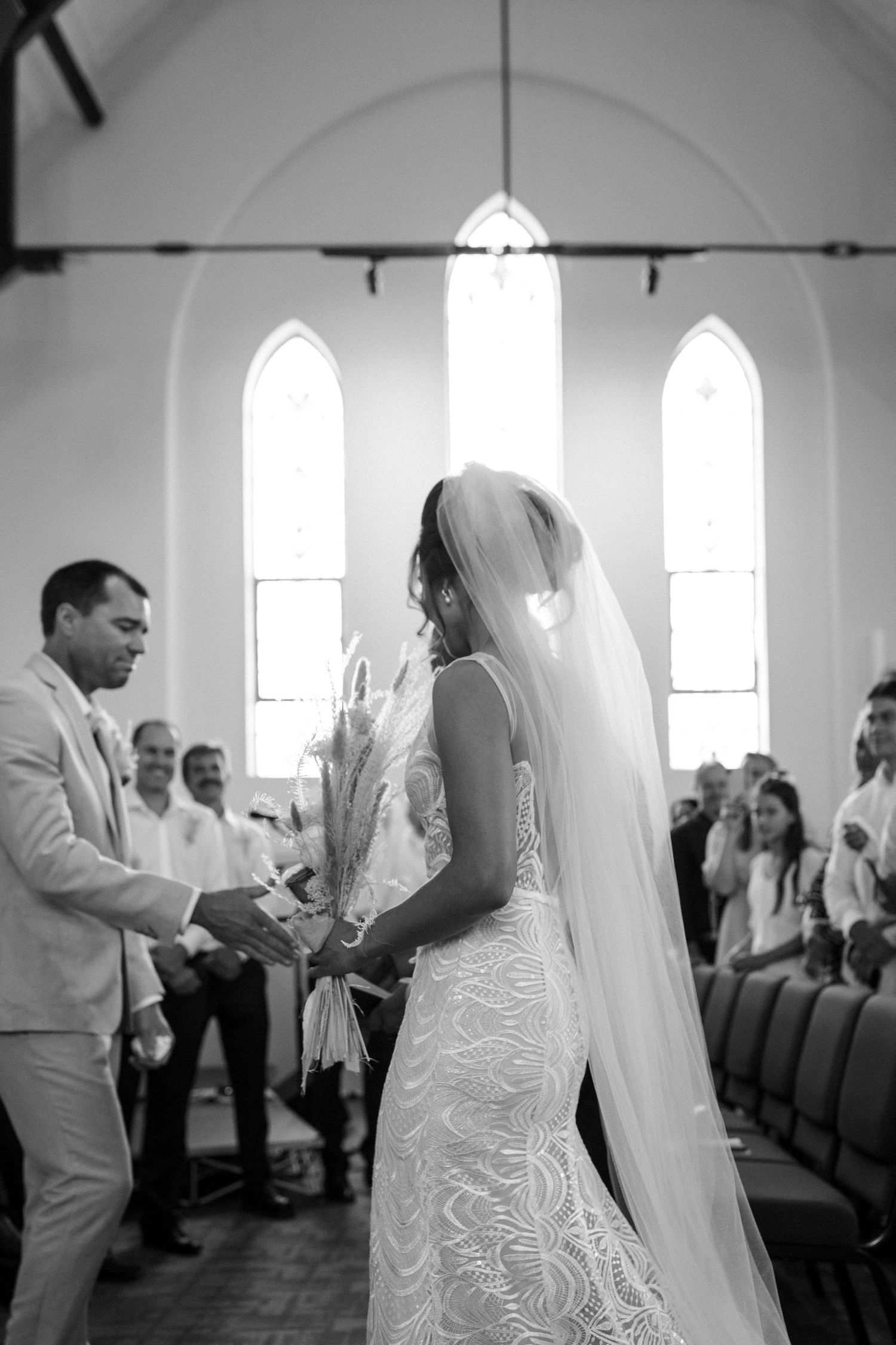 A black and white wedding ceremony photo in front of three church windows.