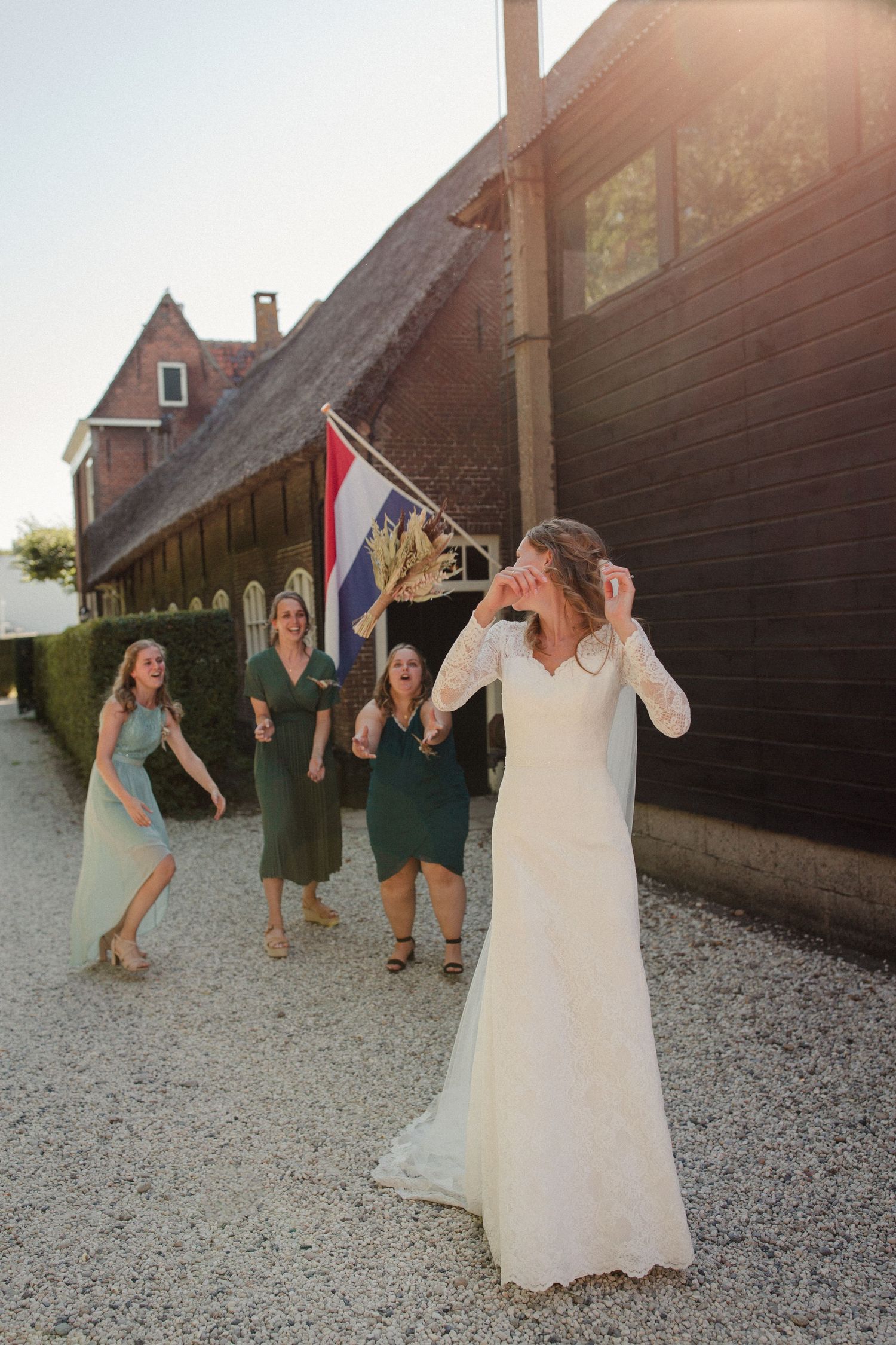A joyful wedding celebration outside a rustic barn with a Dutch flag hanging in the late afternoon sunlight.