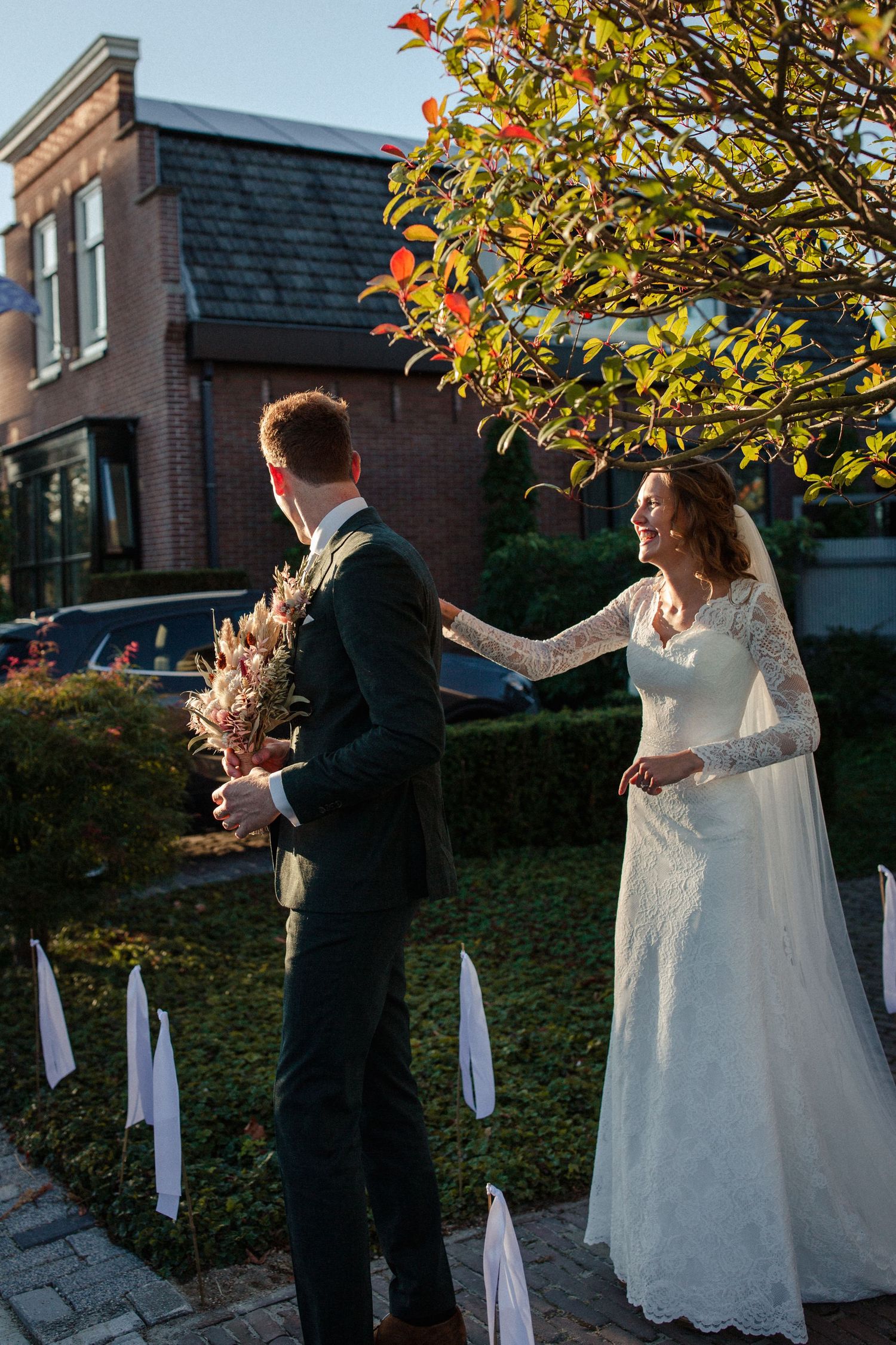 A couple shares a romantic first look moment outside a brick building in autumn as sunlight glows through colorful foliage.