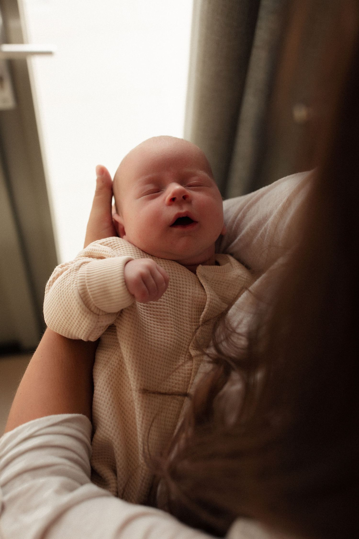 Sleeping baby in cream colored outfit being cradled.