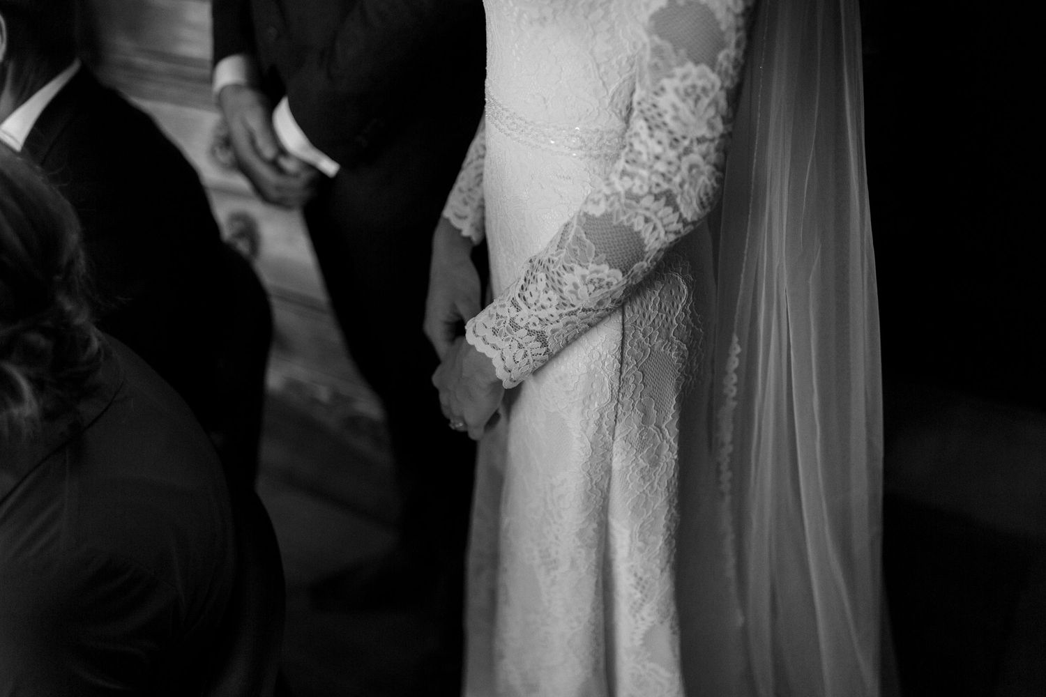 Black and white closeup detail of lace wedding dress and veil at a formal ceremony.