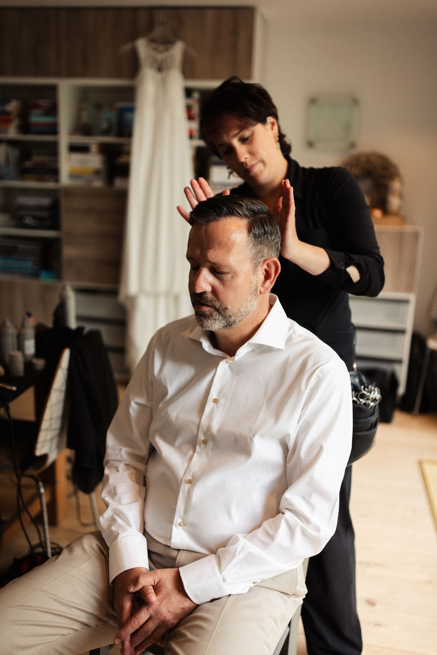 A person receives a relaxing head massage while seated in a room with a white dress visible in the background.