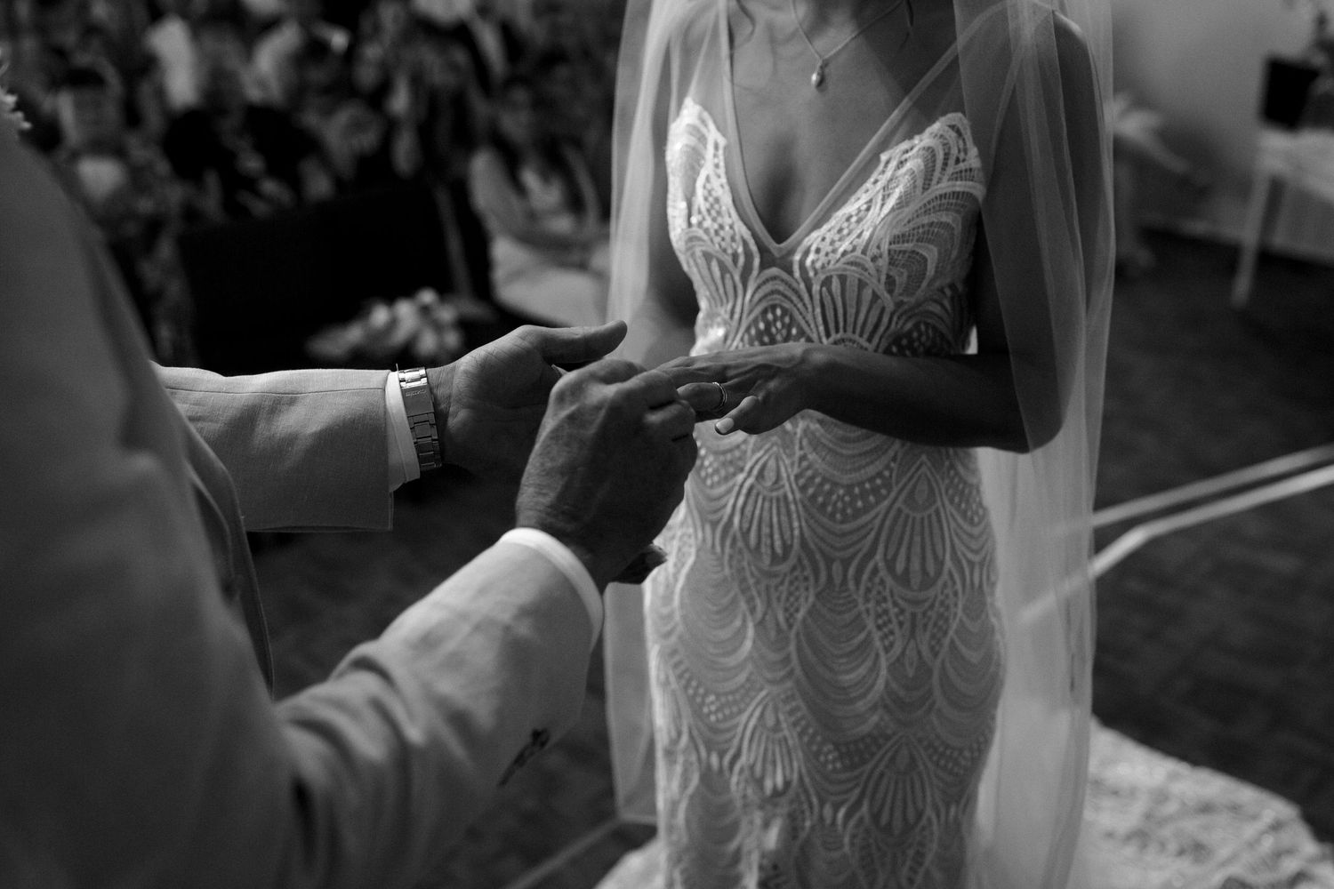 Closeup shot of couple exchanging rings, focusing on bride's detailed lace dress.