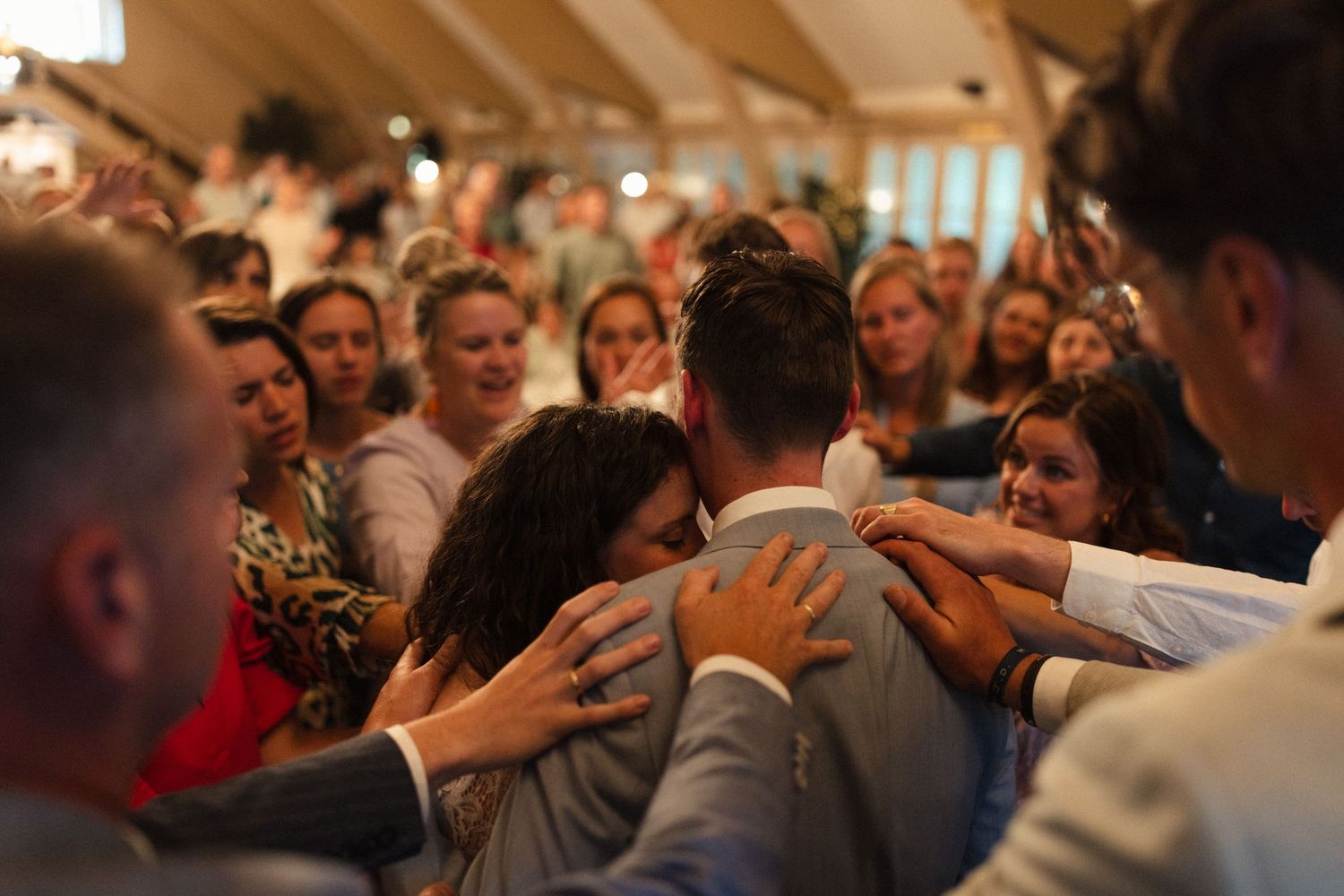 Emotional crowd gathers in circle to embrace and support newlyweds during wedding reception.