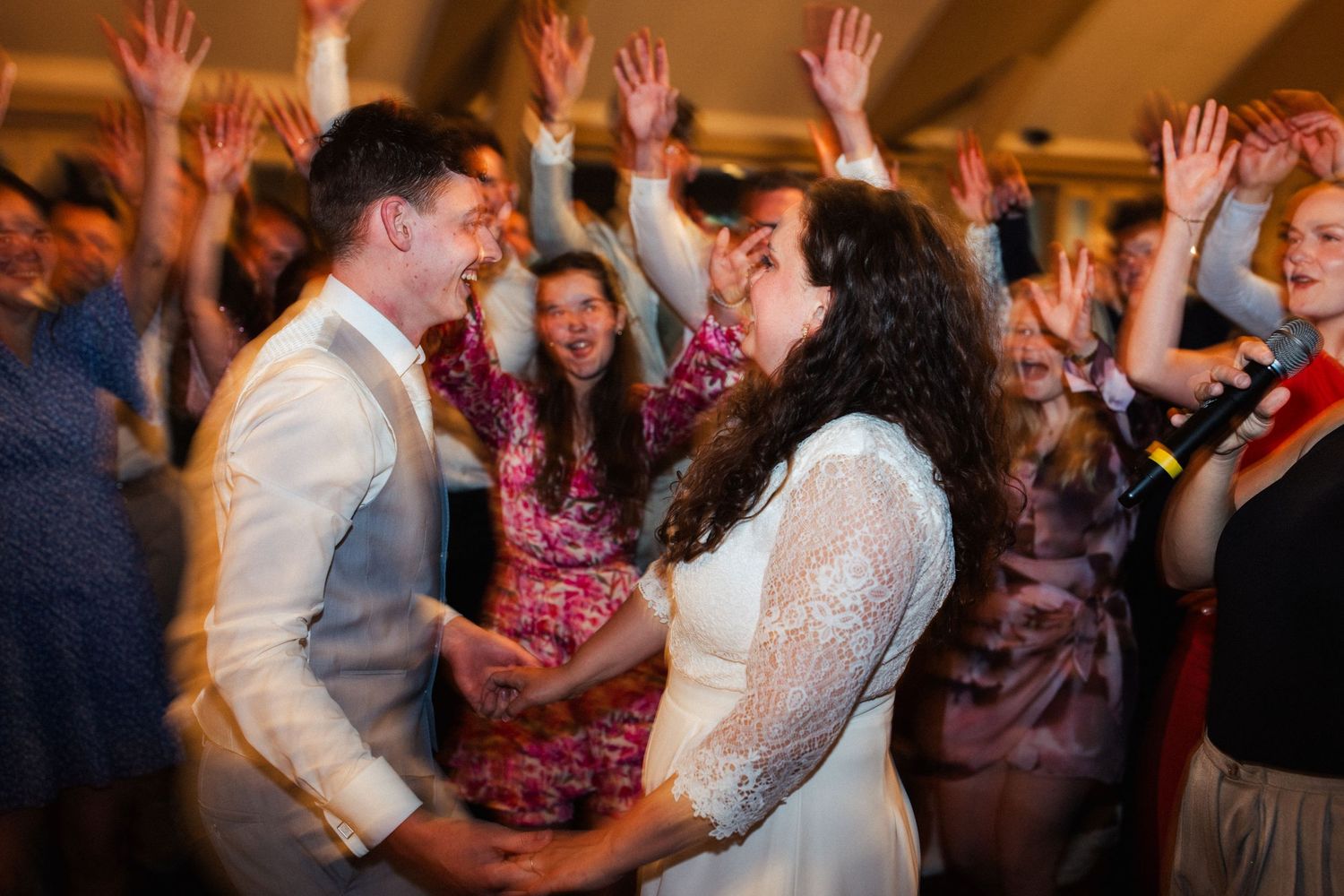 Wedding reception dance party with guests raising hands and celebrating.