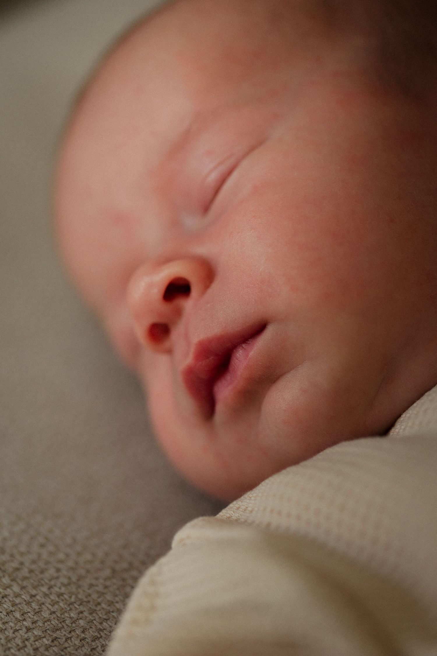 Peaceful close-up of a sleeping newborn baby's face against soft fabric.