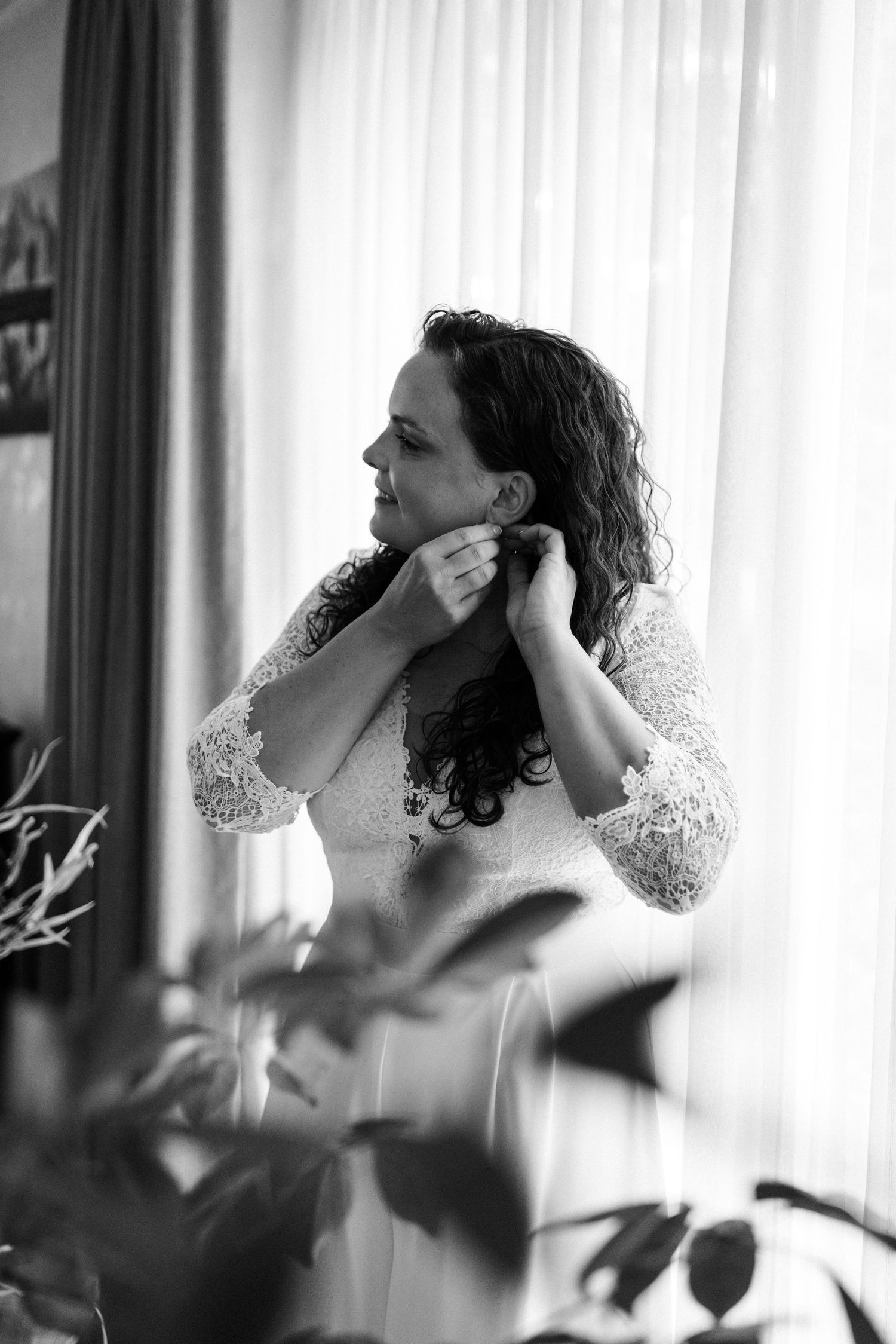 Black and white photo of person in lace dress getting ready by a window.