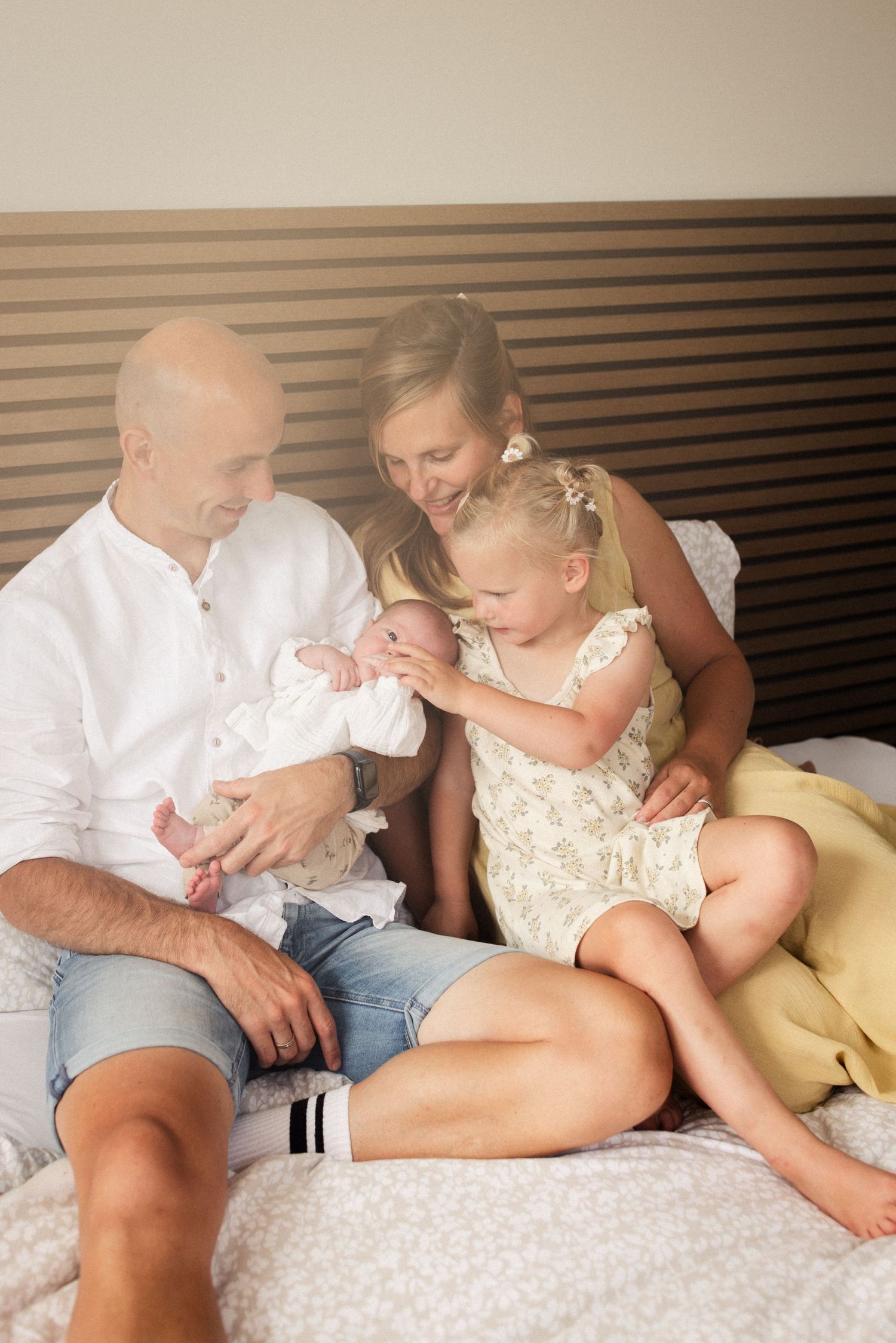 Papa, mama, grote zus en een piepklein baby'tje samen op bed.