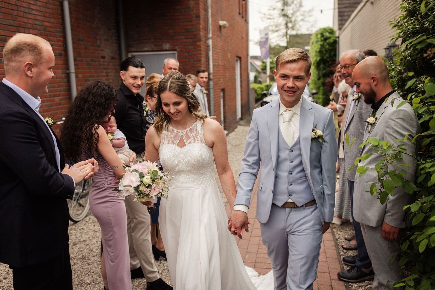 A bride and groom celebrate joyfully with their wedding party outside a brick building.