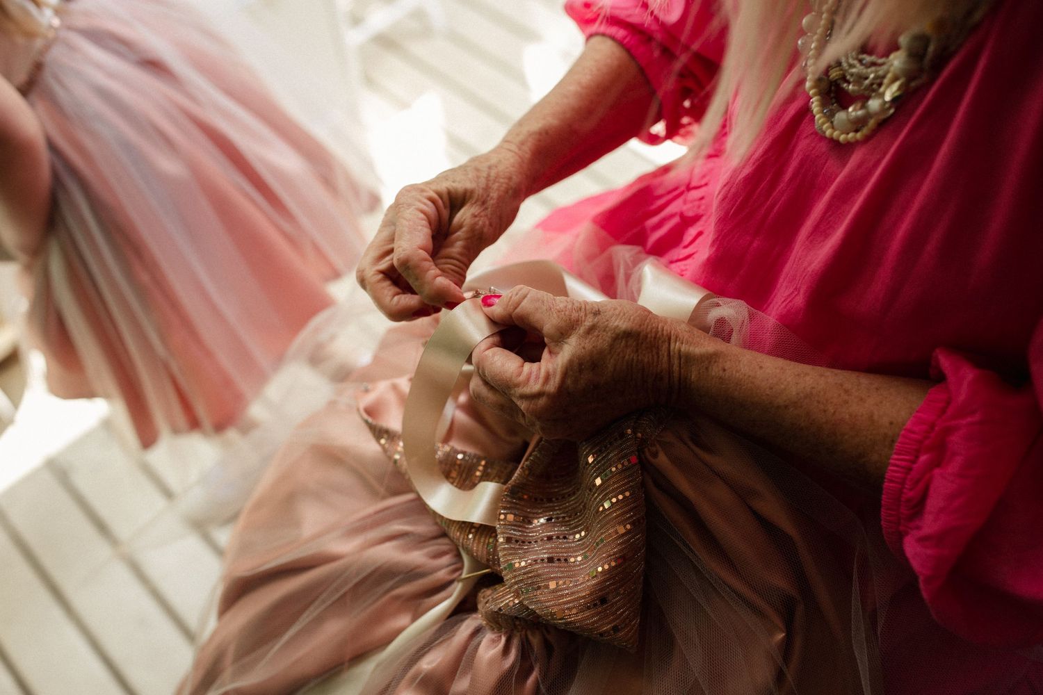 Hands sewing delicate details on a pink dress.