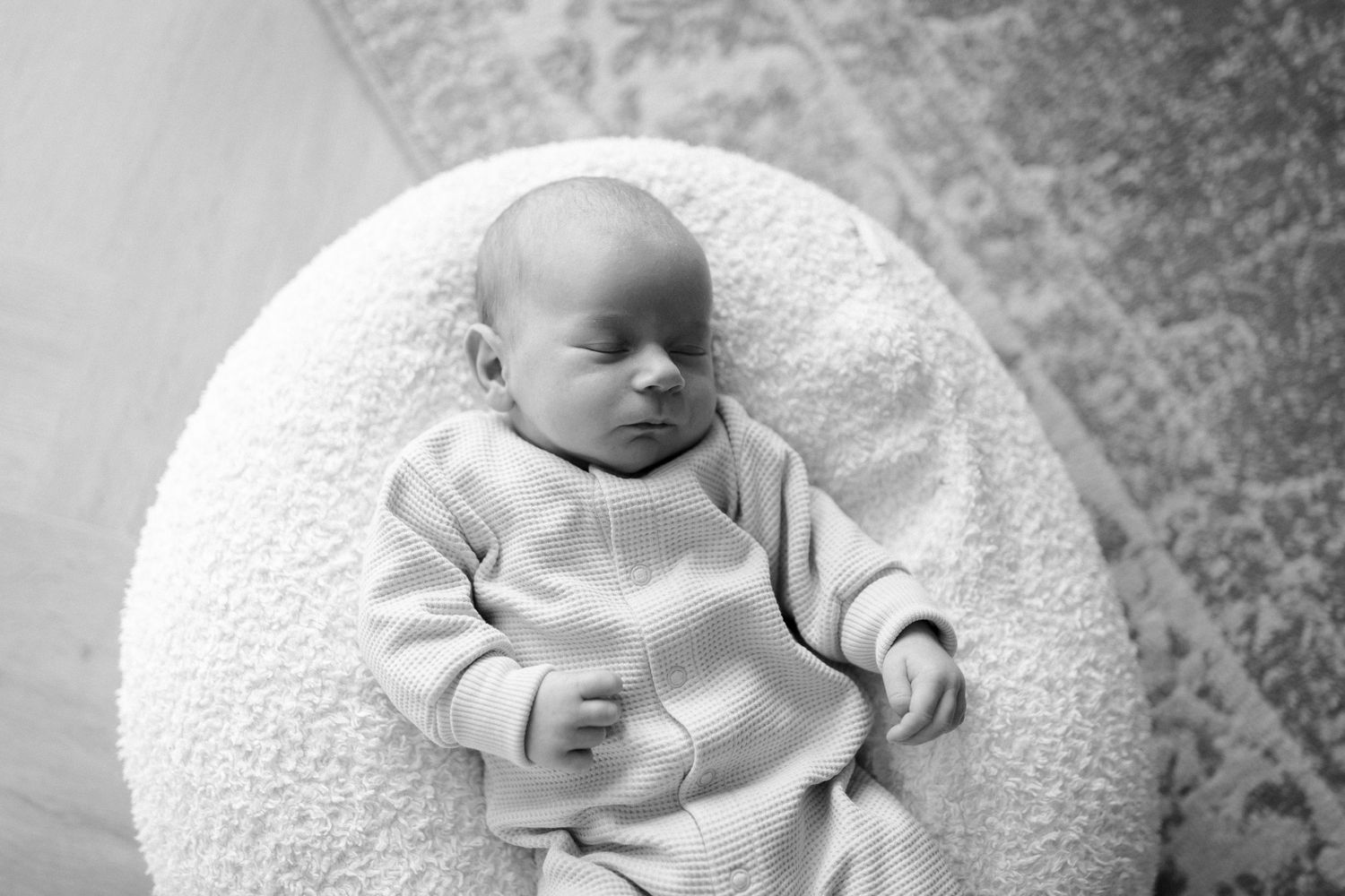 Baby napping on white circular cushion in neutral toned outfit.