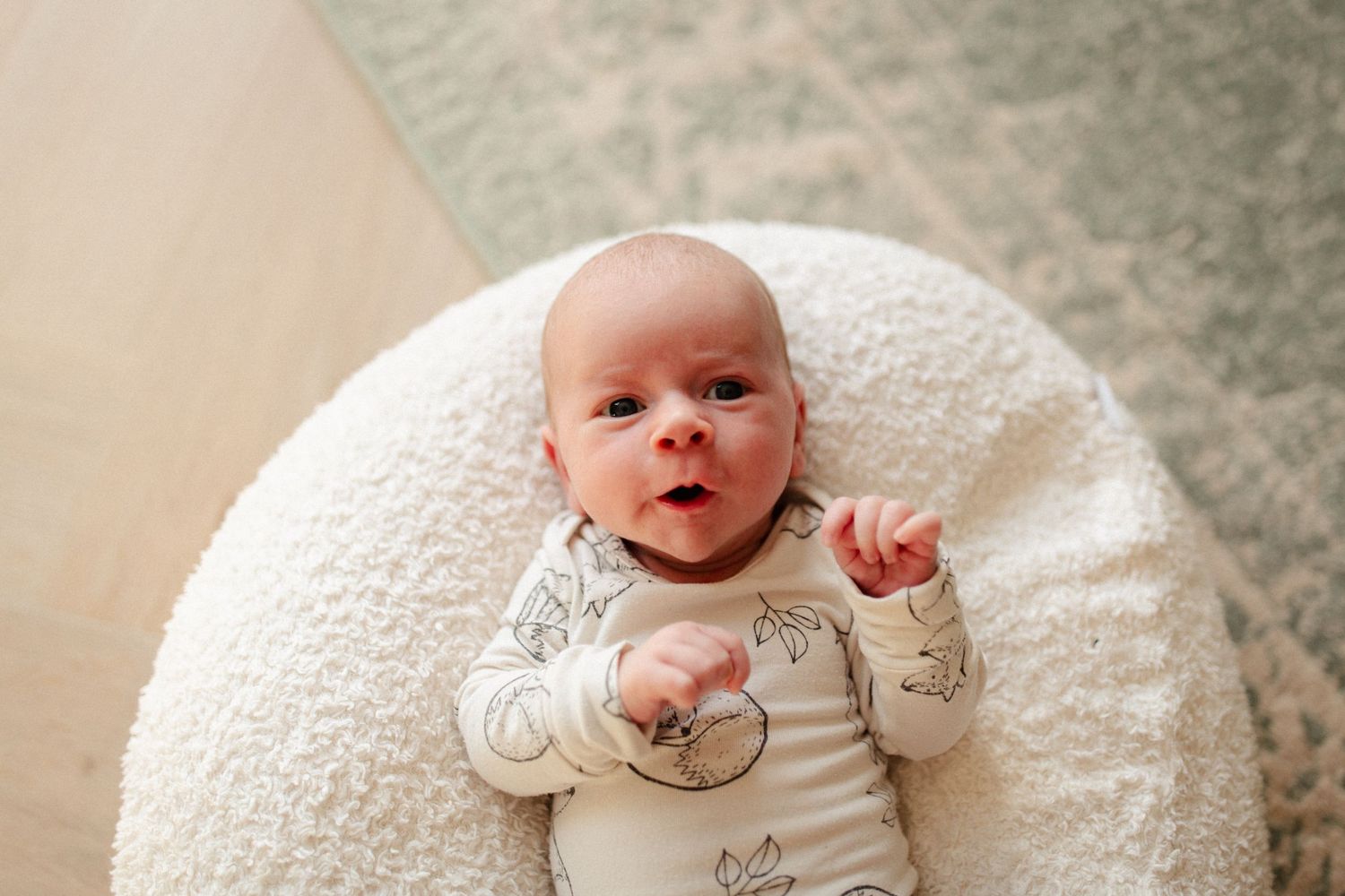 Infant lying on white cushion wearing light colored onesie.