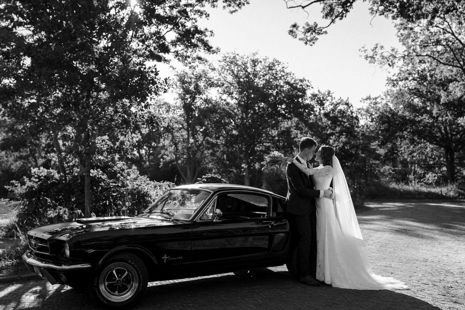 Classic black vintage Mustang car parked on a wooded path during an elegant outdoor wedding photoshoot.