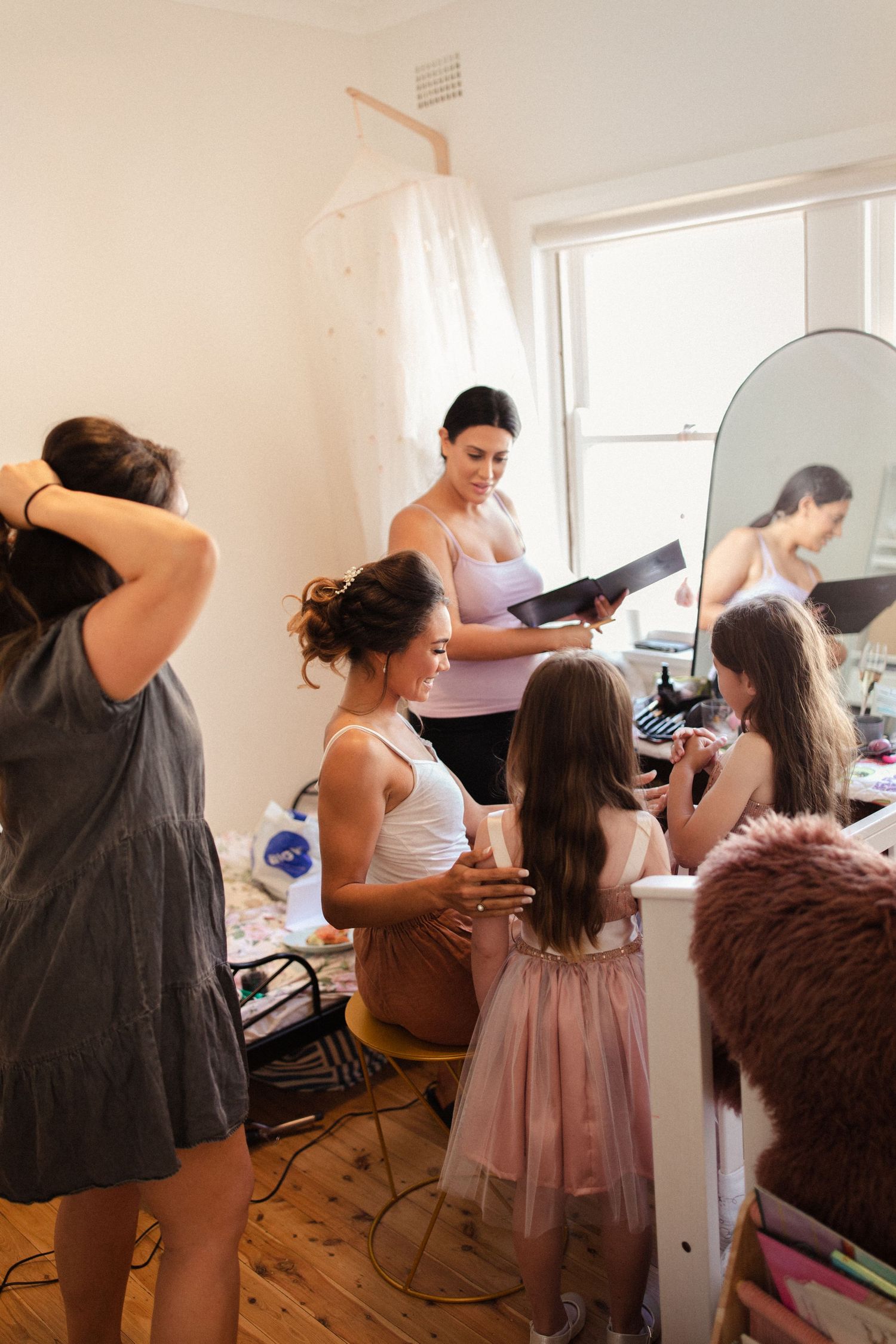 Wedding preparation scene in a bright room with a white dress hanging and people getting ready for the special day.