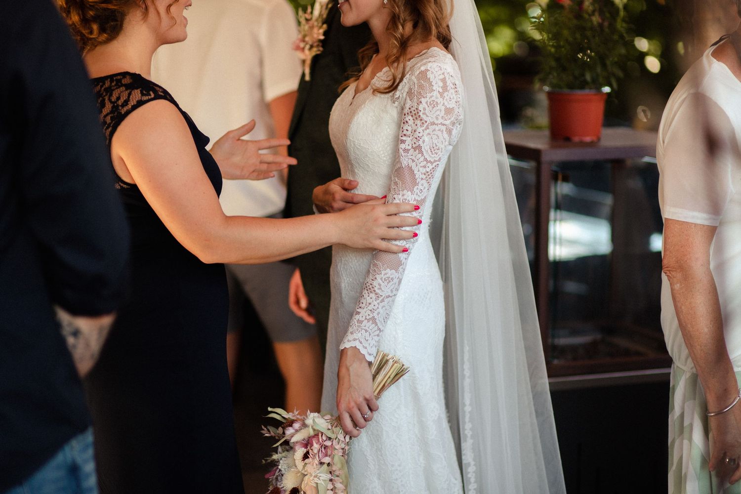 Elegant lace wedding dress with flowing veil shown from the side with delicate bouquet details.