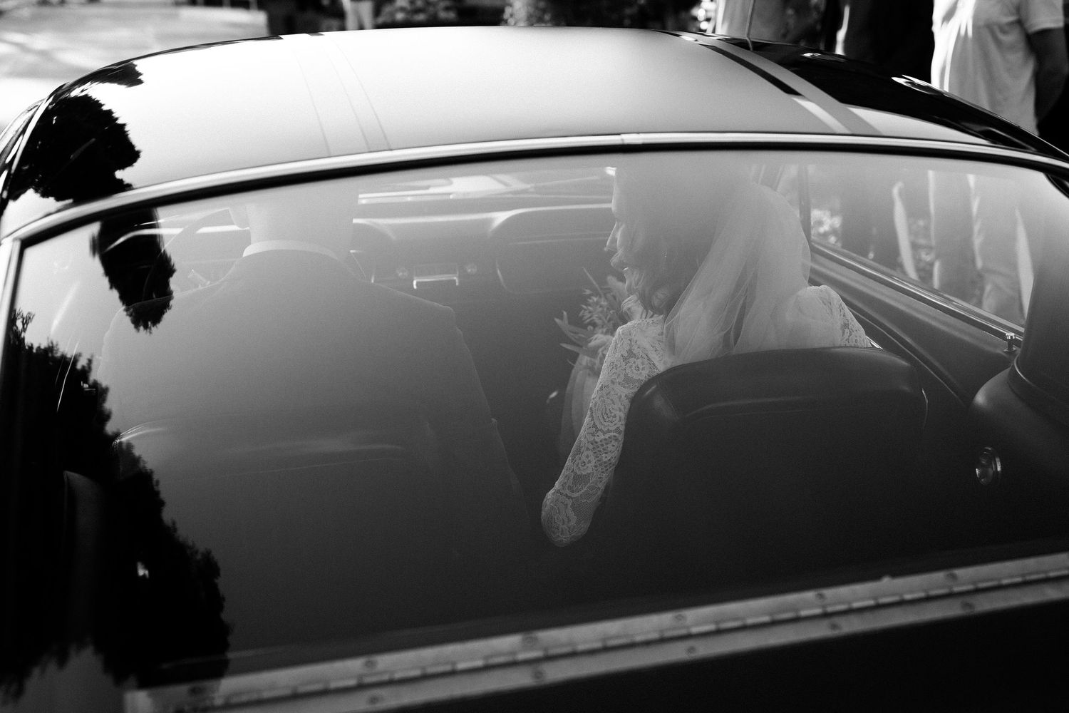 A black and white photograph showing glimpses of a passenger through a car window with reflections on the glass.