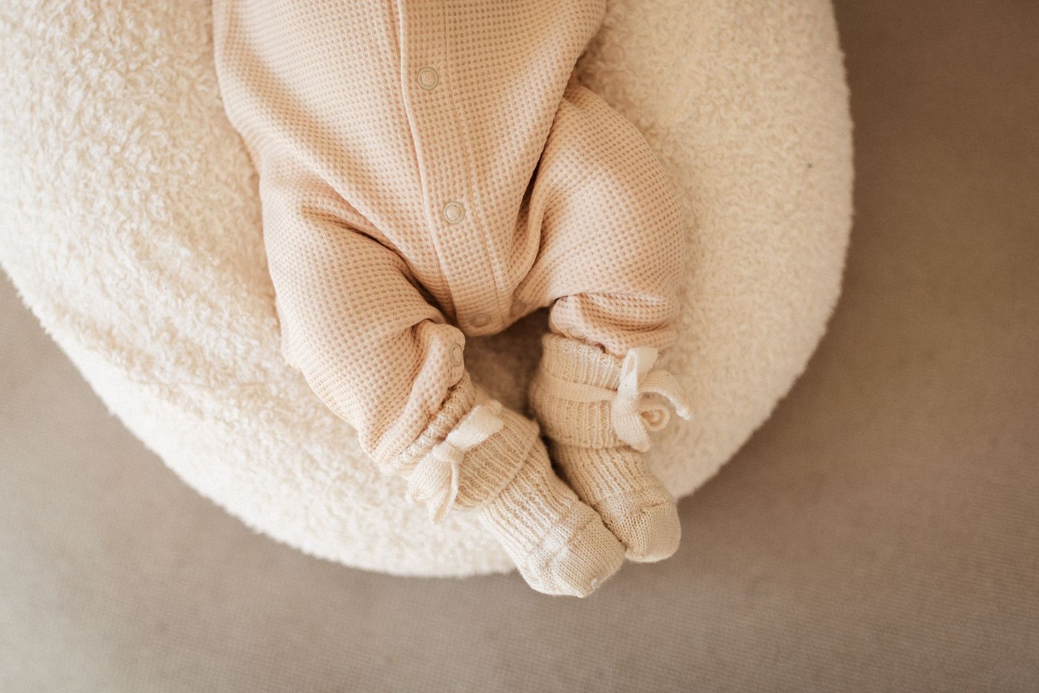 Close-up of baby feet in beige knit booties on white cushion.