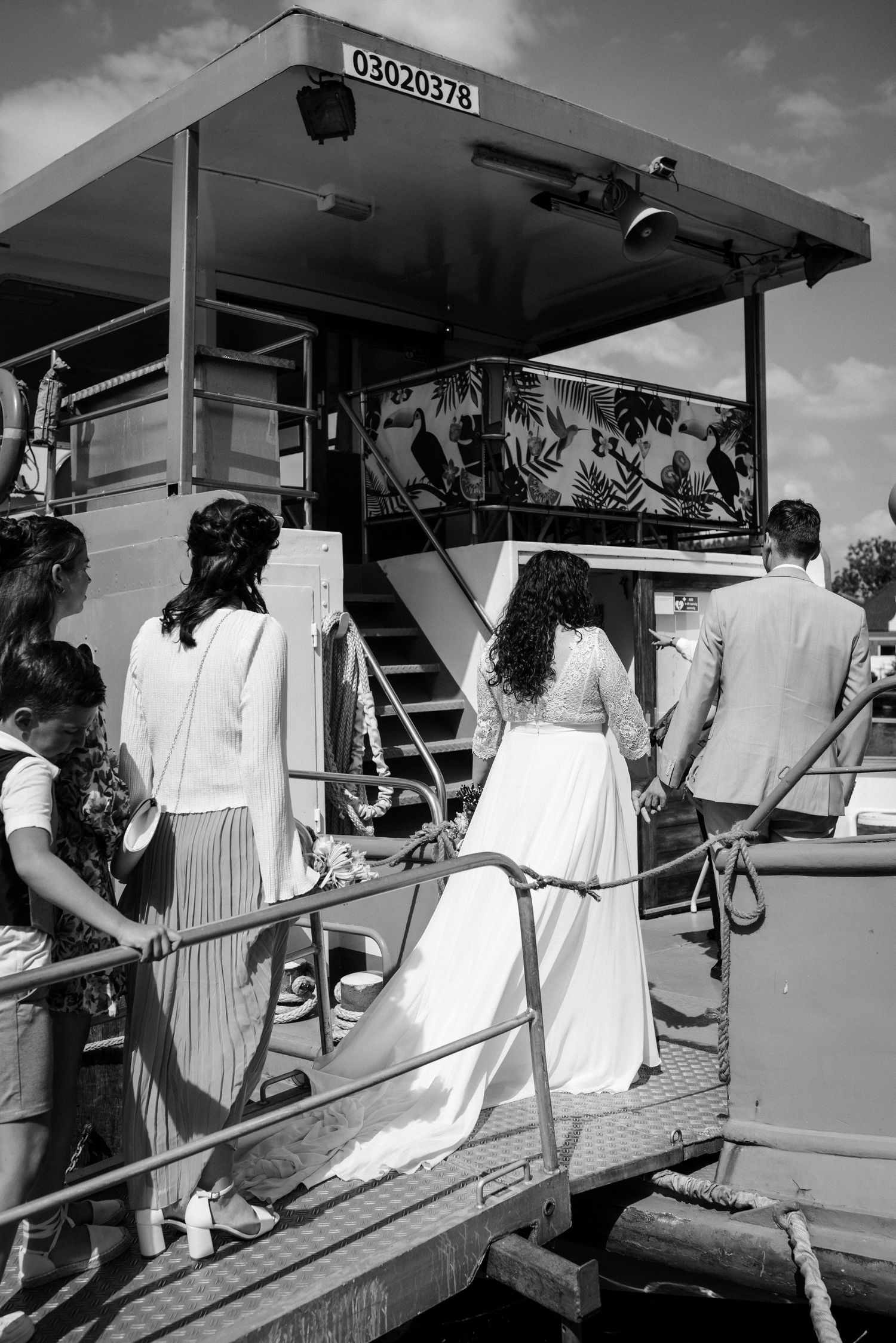 People in white clothing boarding a vintage boat at a dock in a black and white photograph.