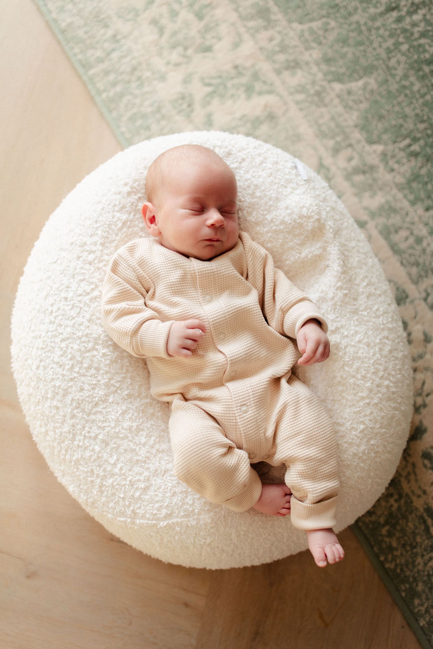 Infant in beige onesie sleeping peacefully on round white cushion.
