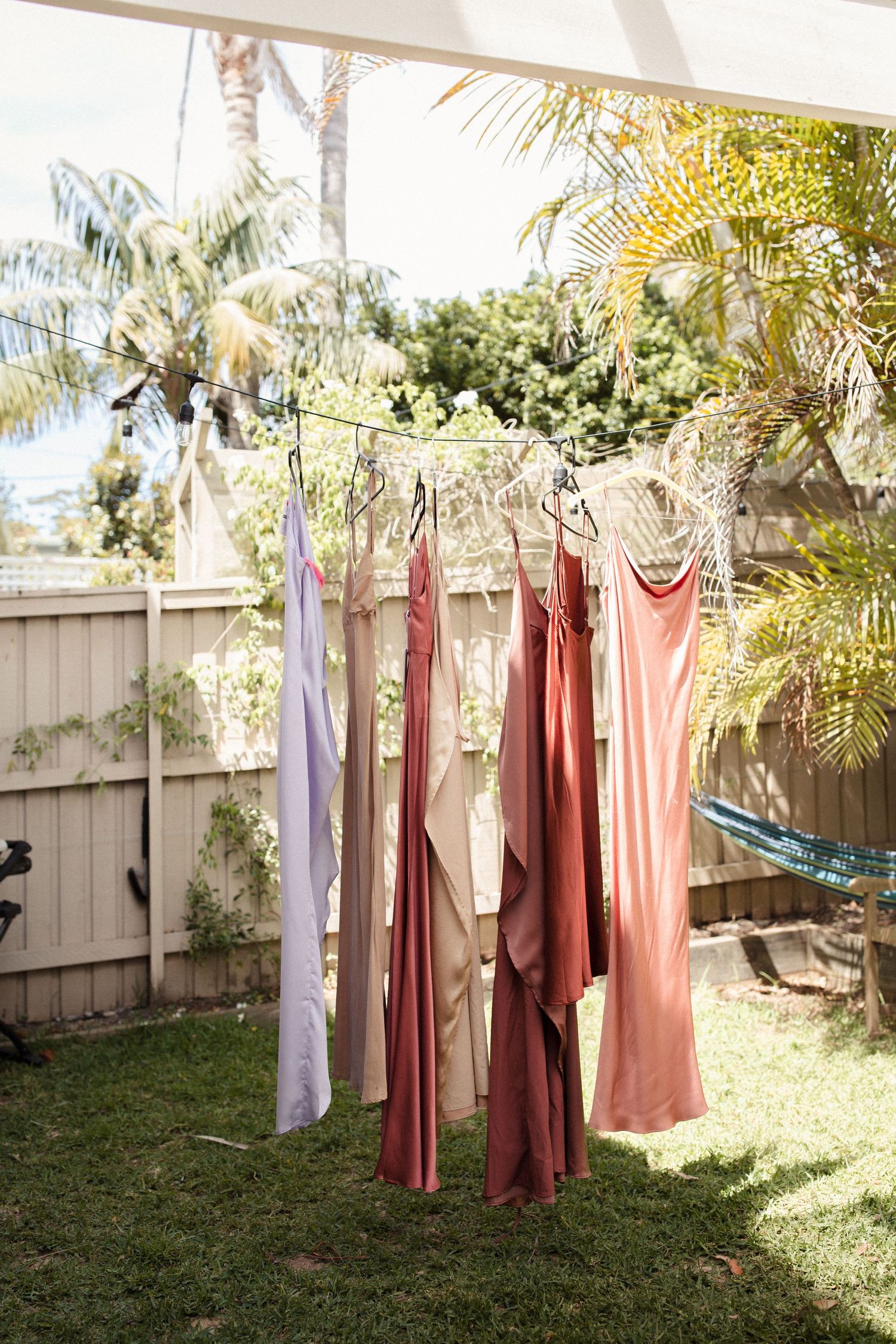Pastel dresses hanging on a clothesline in a sunny tropical garden.