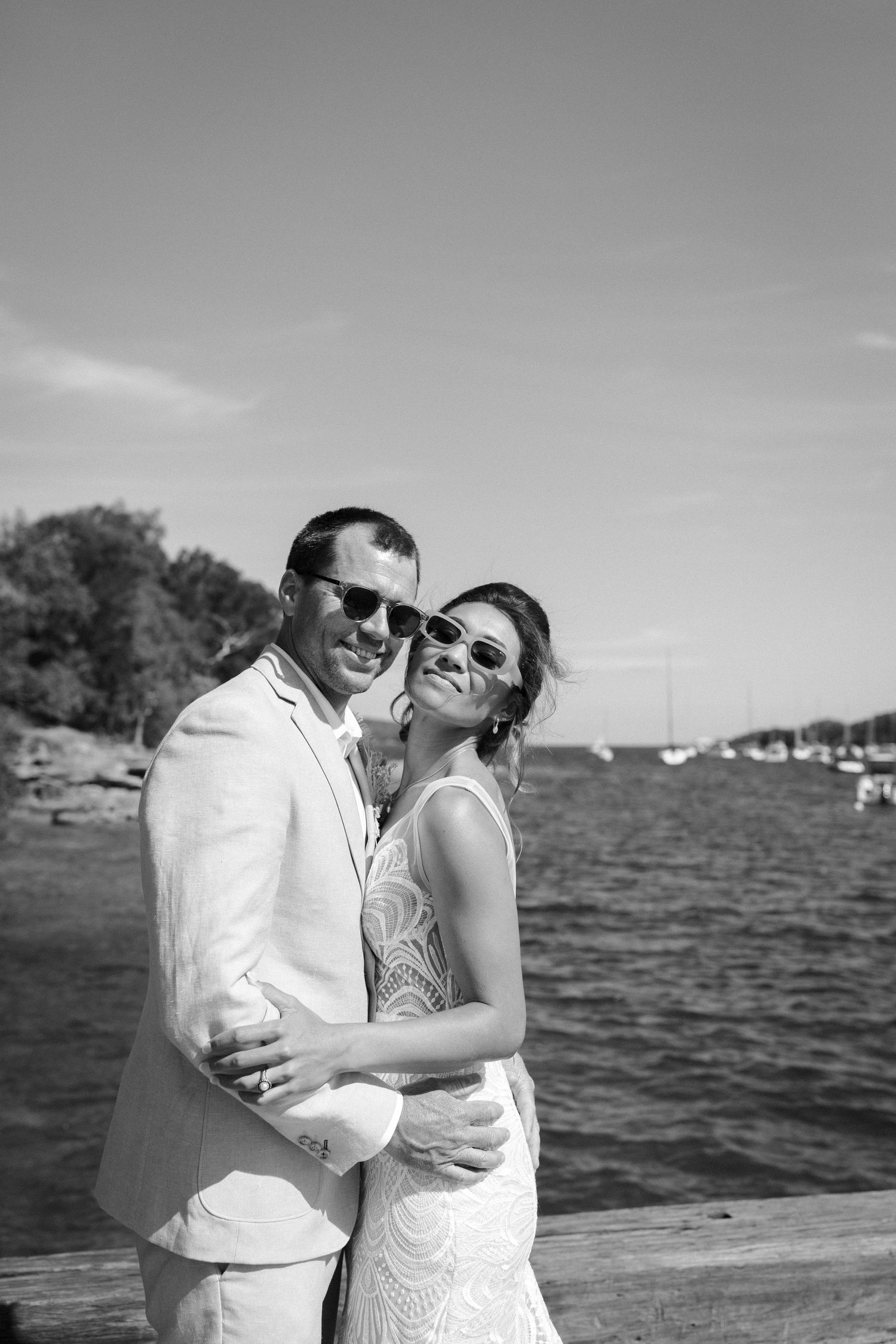 A romantic black and white portrait of a couple embracing by the water.