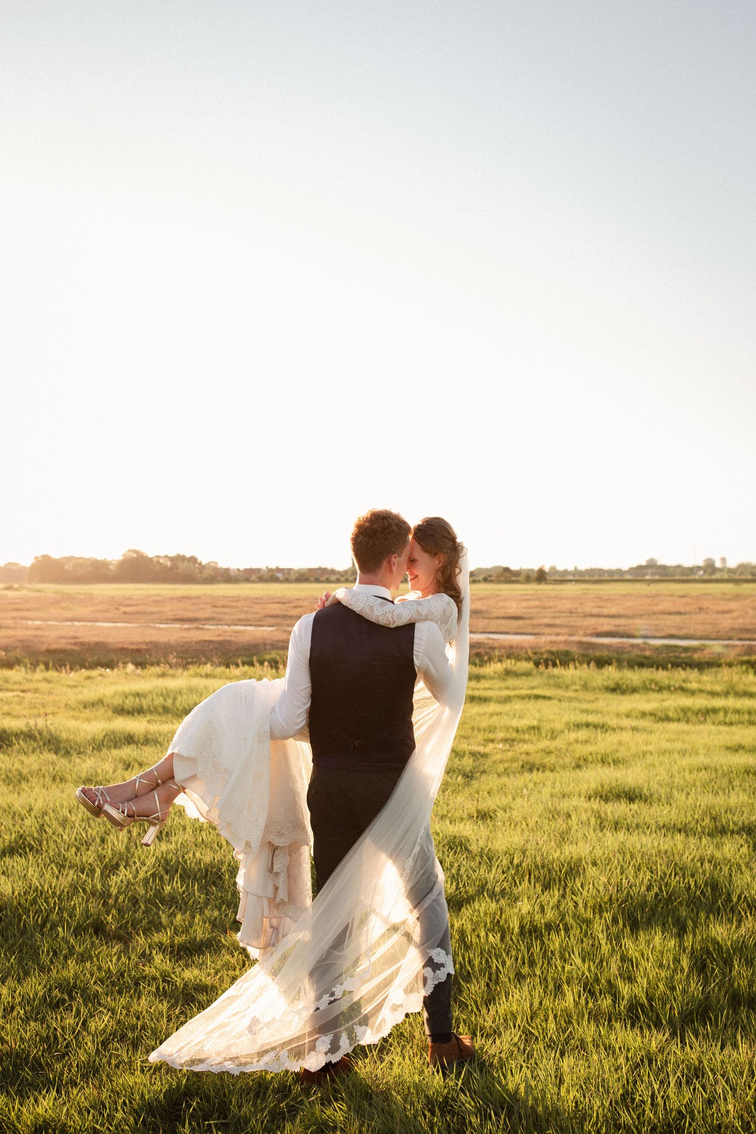 A romantic couple in wedding attire embrace in a sunlit meadow at golden hour.