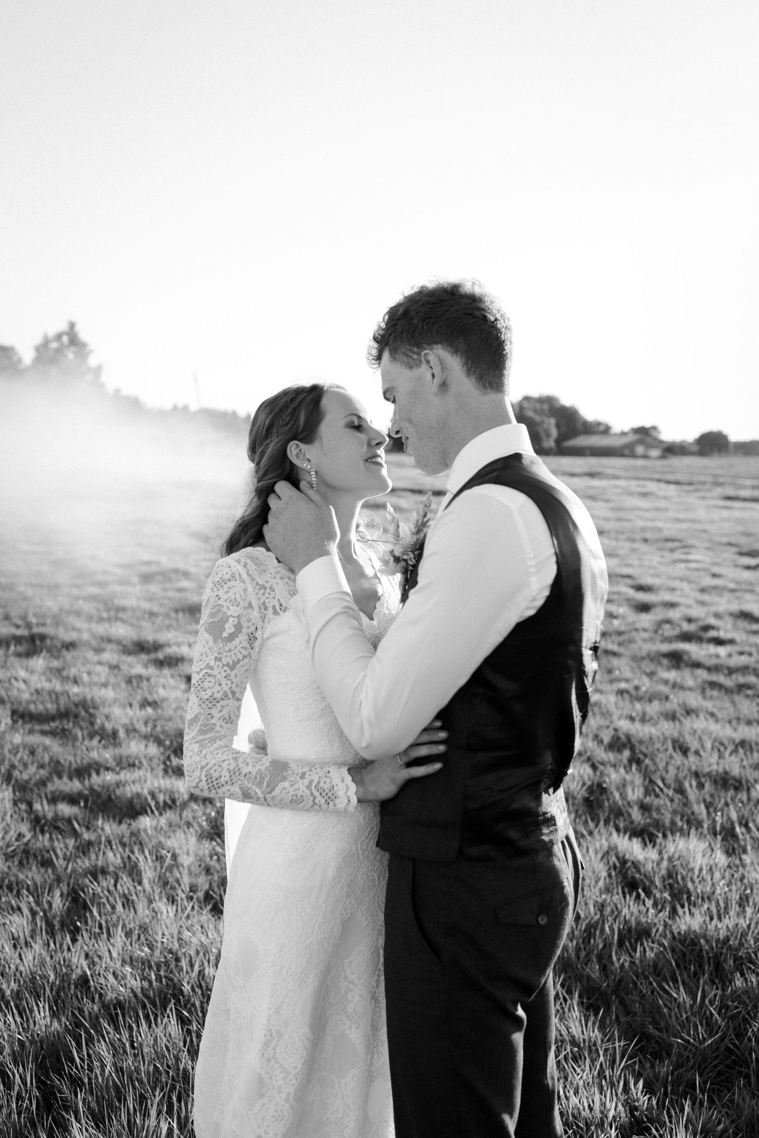 A romantic black and white wedding photograph of a couple embracing in a sunlit meadow.