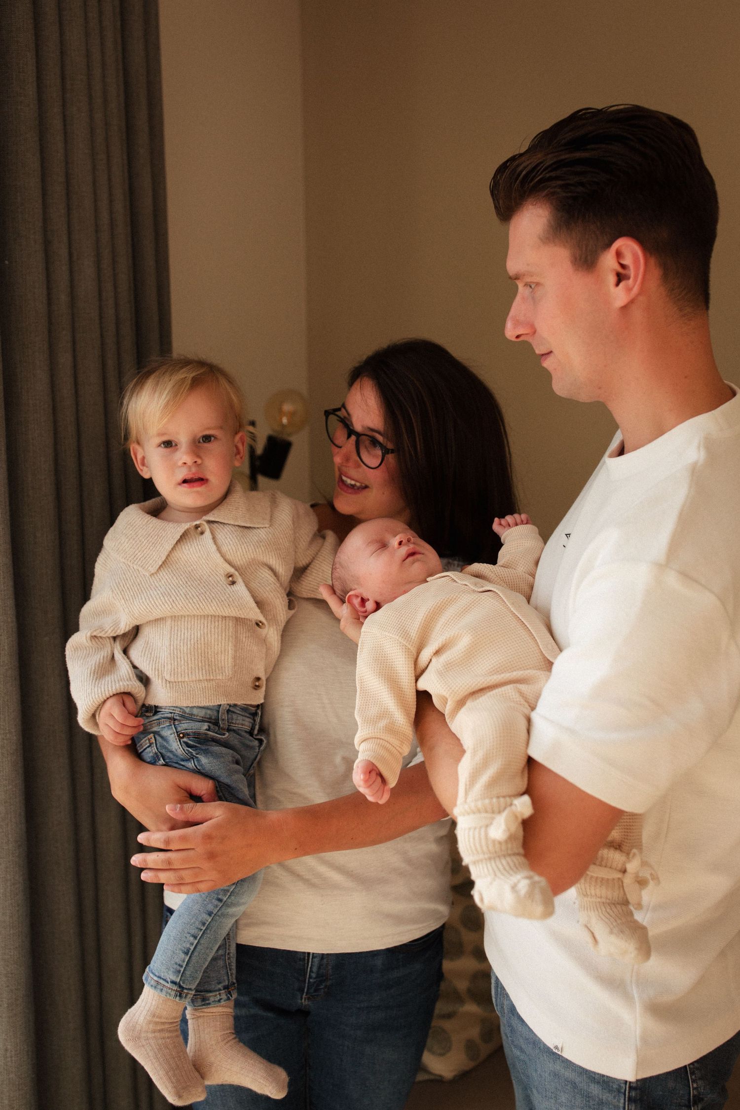 Family portrait with toddler and newborn in coordinated neutral outfits.