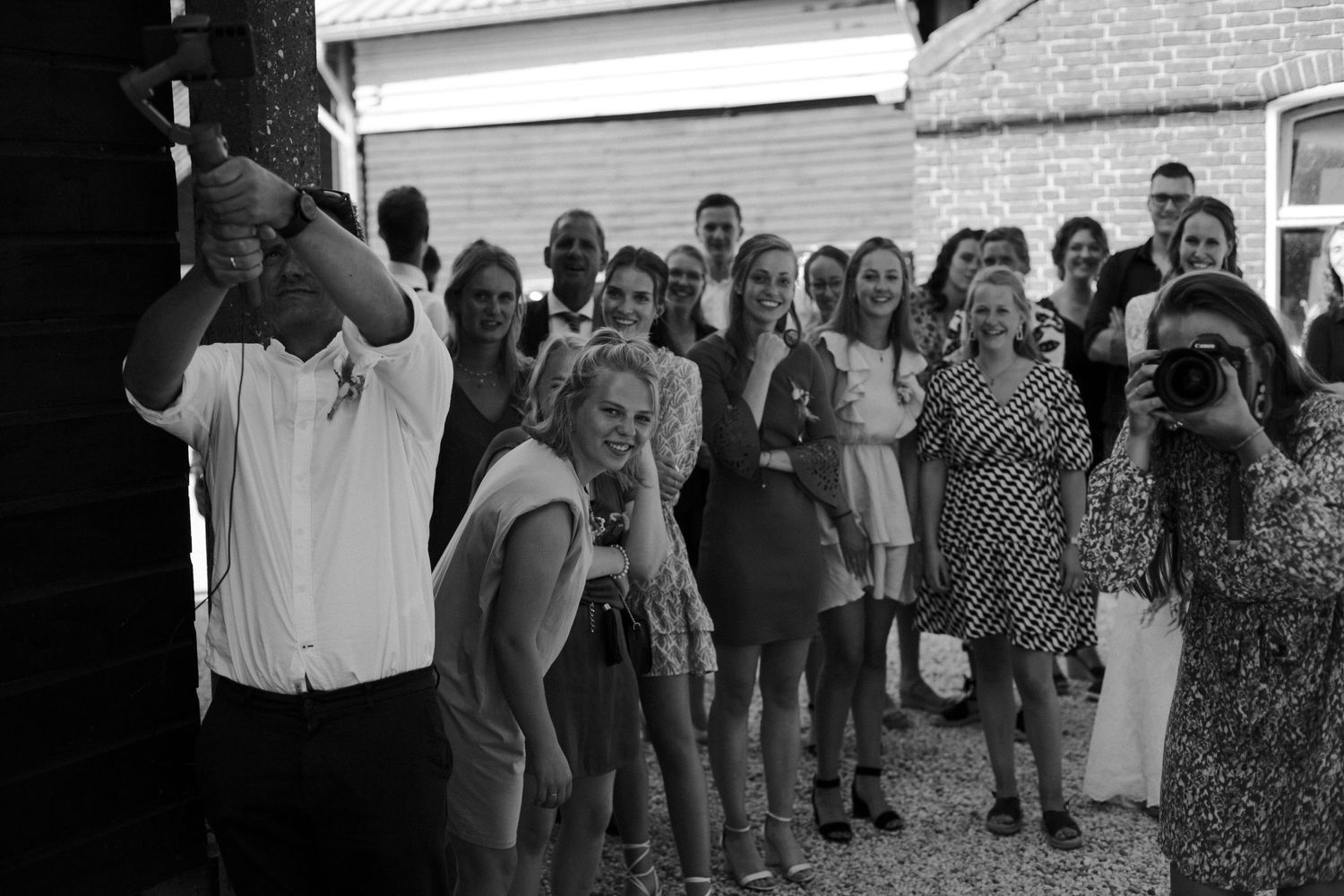 A black and white photograph of a group of people gathered outdoors near a brick building.