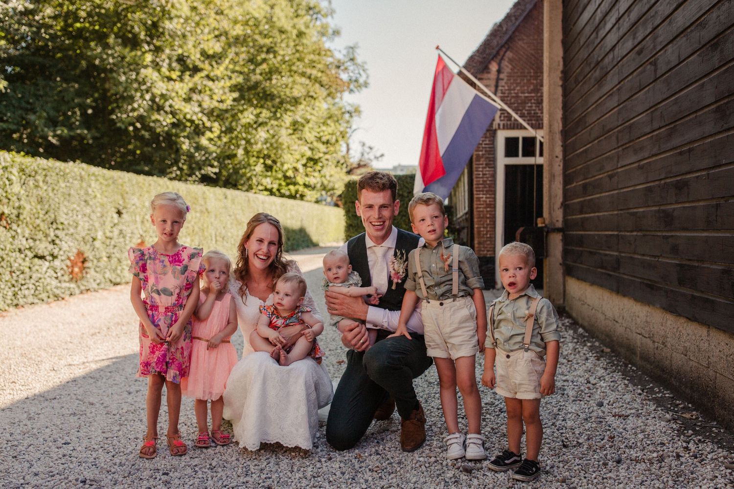 A group poses together outside a rustic wooden building with a Dutch flag displayed in the background.