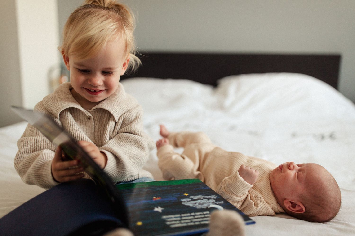 Children sitting together on bed while looking at picture book.