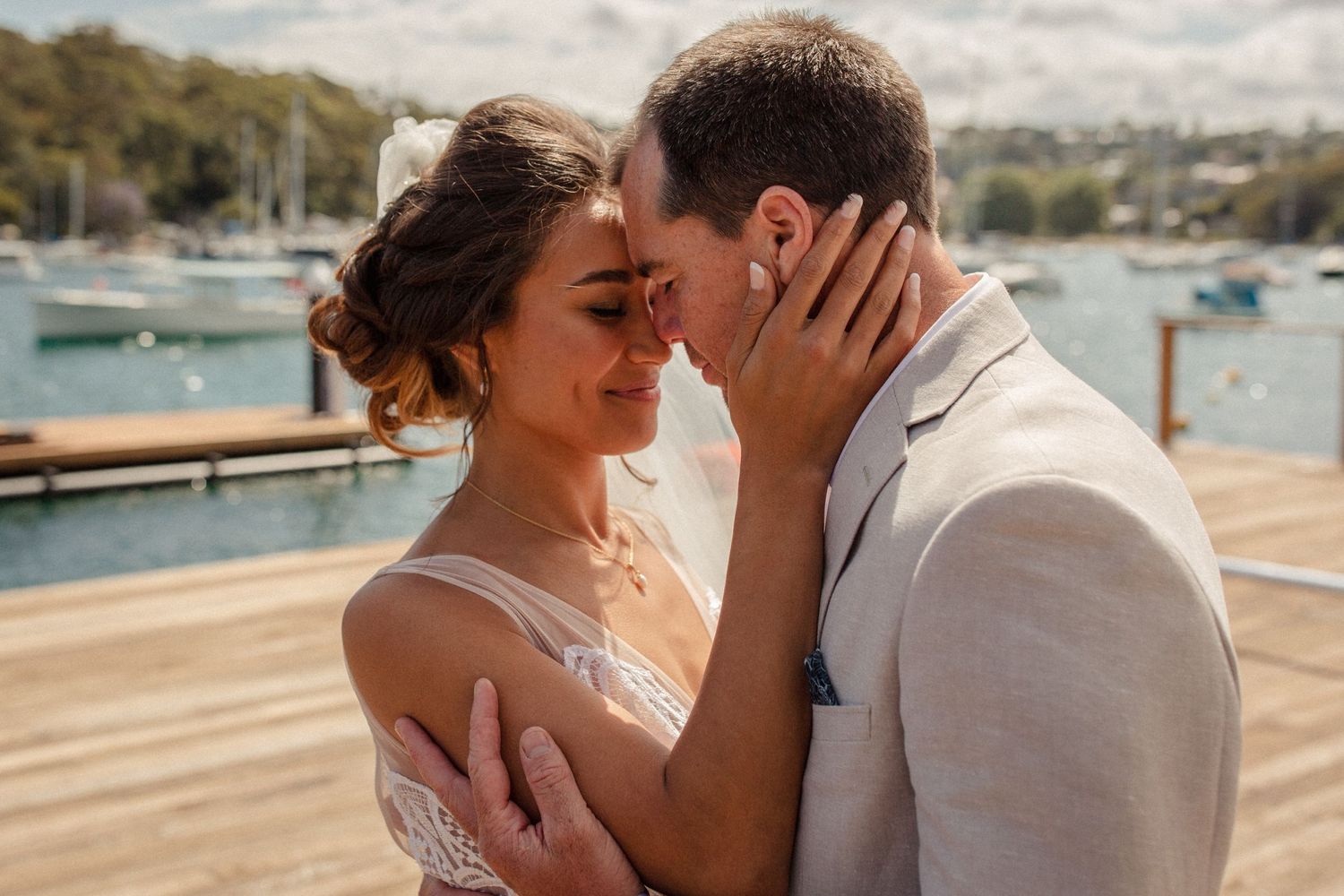 A romantic moment between newlyweds embracing on a marina dock with boats in the background.