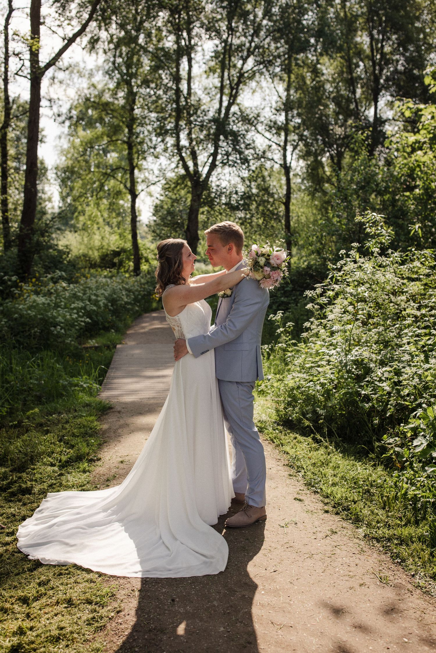 Newlyweds share an intimate moment on a sun-dappled forest path.