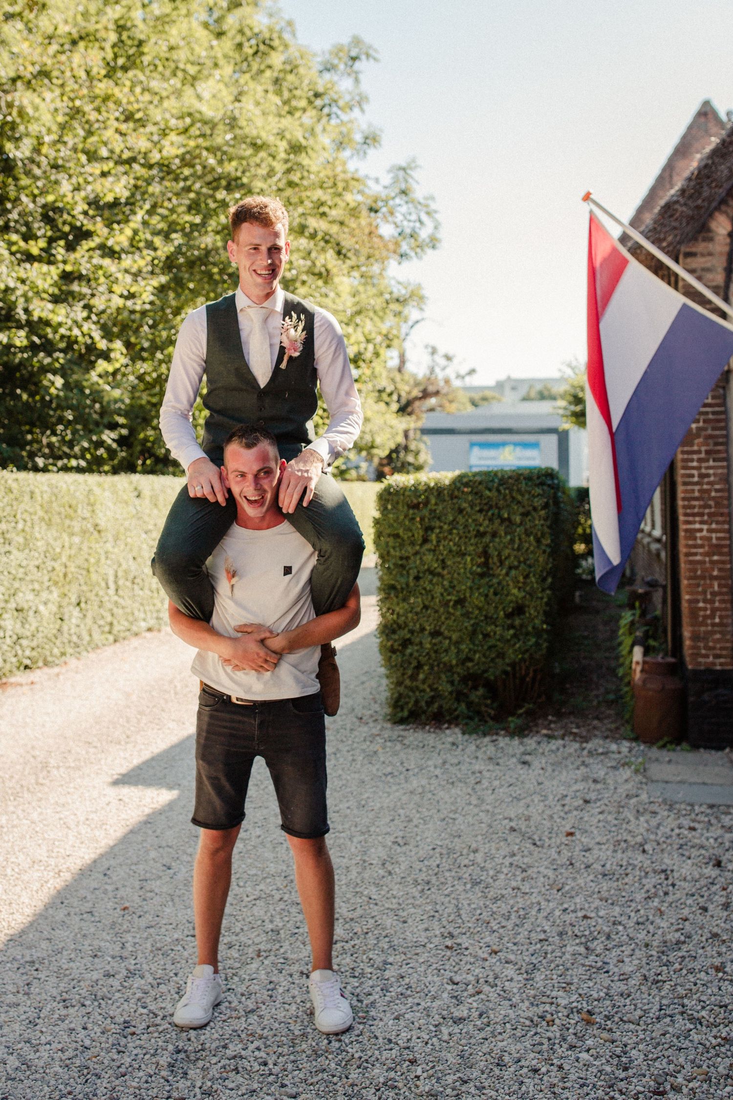Two people having fun outdoors with one giving a piggyback ride, with a Dutch flag visible in the background.