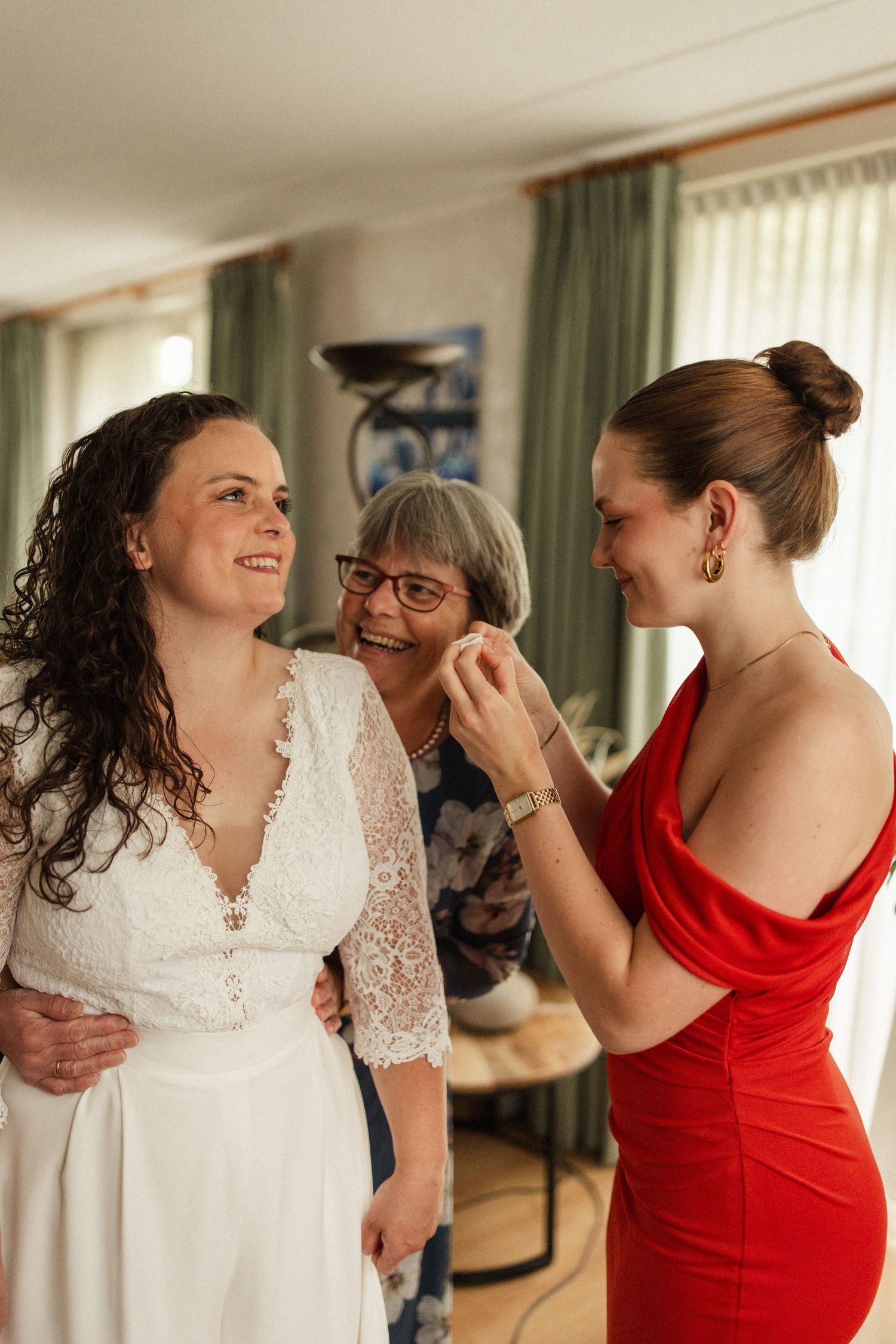 Three people share an intimate moment while getting ready in a room with green curtains and natural lighting.