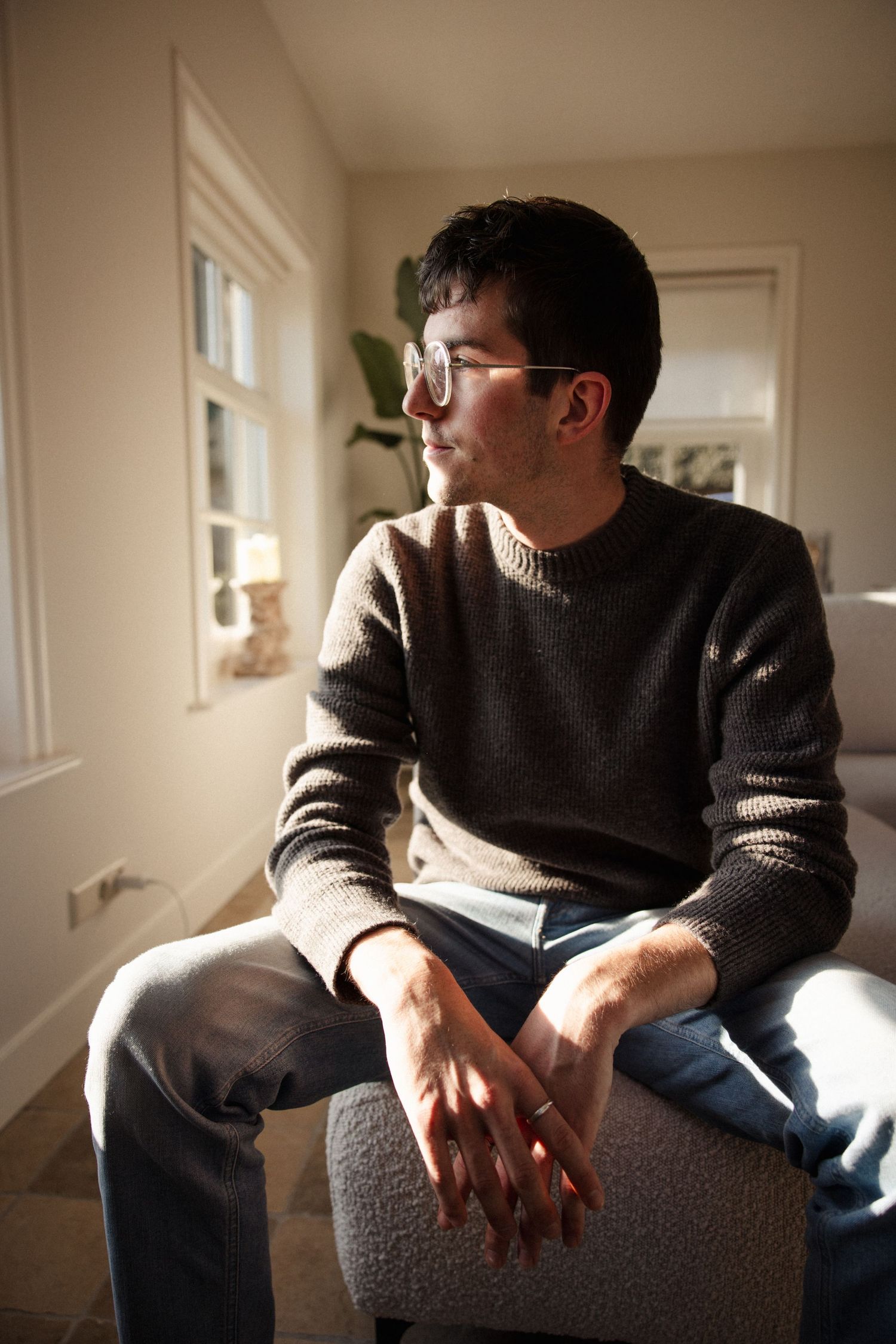 Contemplative figure sitting by window in cozy sweater with natural lighting.