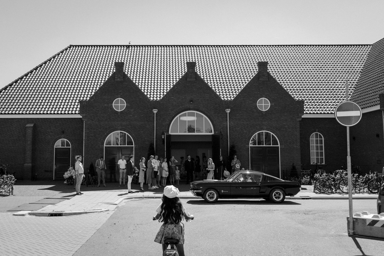 Vintage black and white photograph of a train station exterior with classic architecture and a car parked outside.