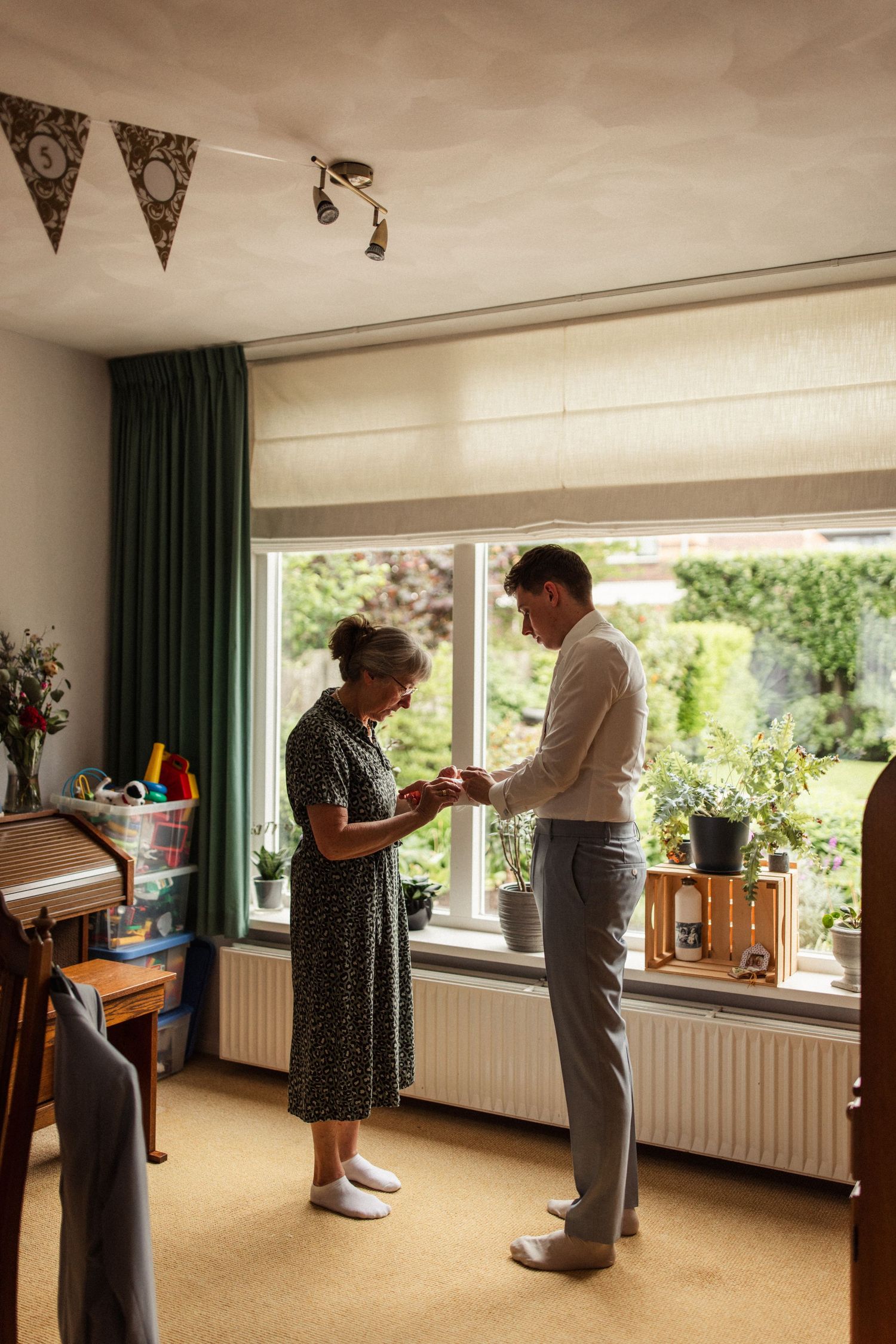 Two people stand by a window with bunting decorations during wedding preparations.