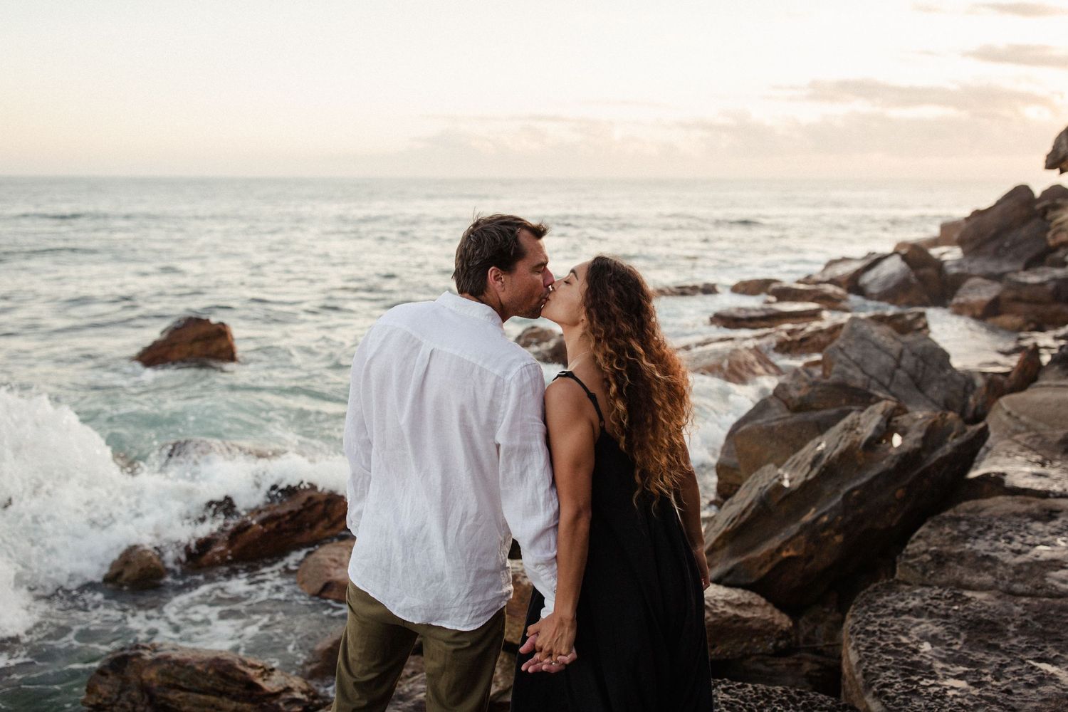 Romantic coastal scene with couple on rocky shore at sunset.