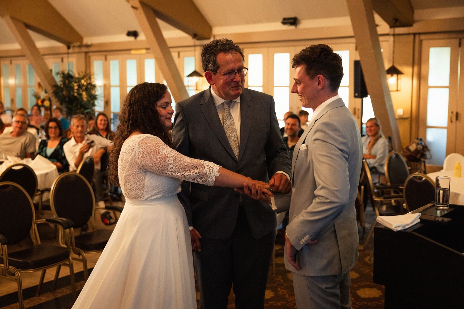 An officiant stands between a bride and groom during their indoor wedding ceremony.