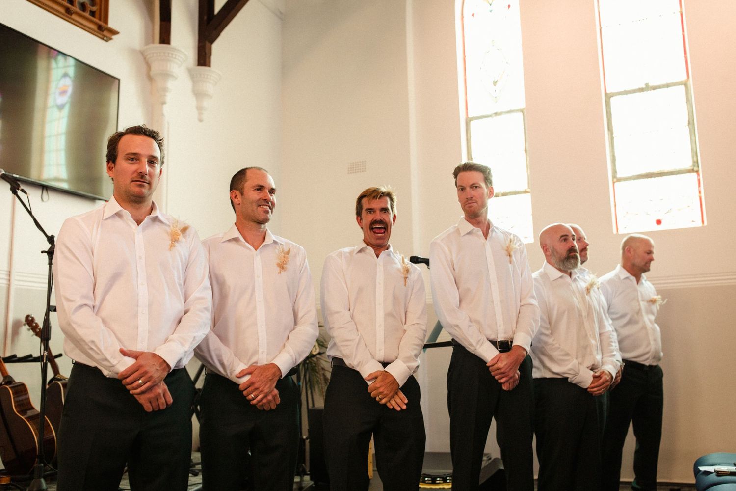 Groomsmen line up in white shirts and dark pants at the front of a traditional church.