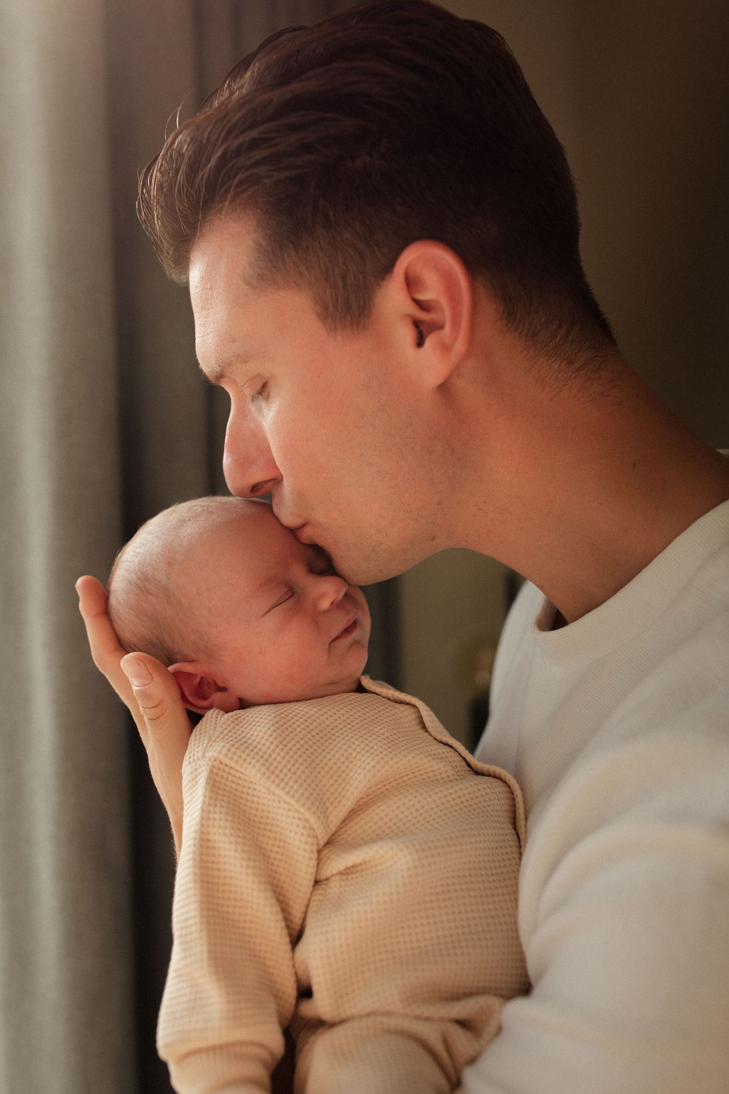 Tender moment between parent and sleeping newborn in soft natural light.