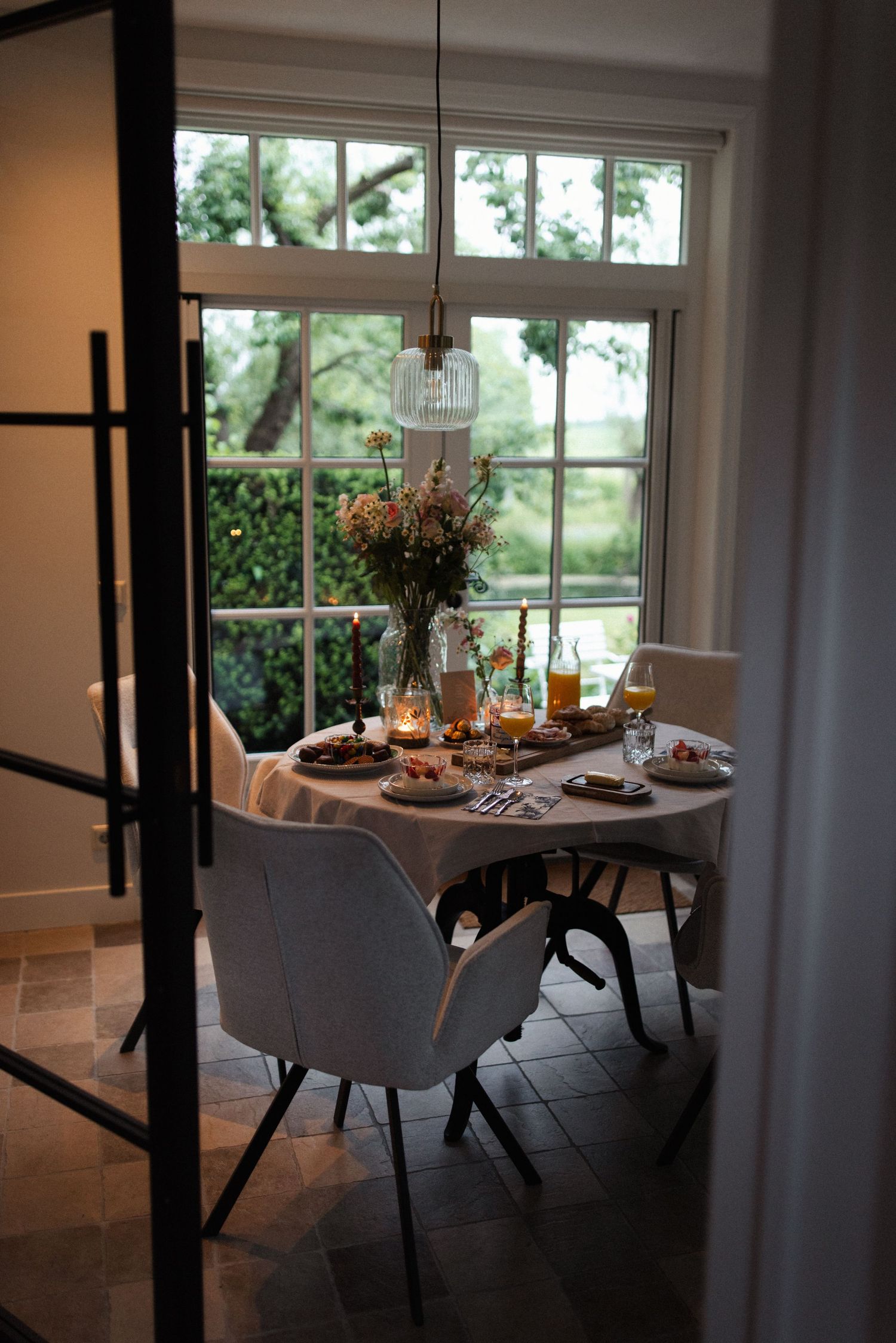 Cozy dining nook with grey chairs and table set for a meal next to large windows overlooking lush greenery.