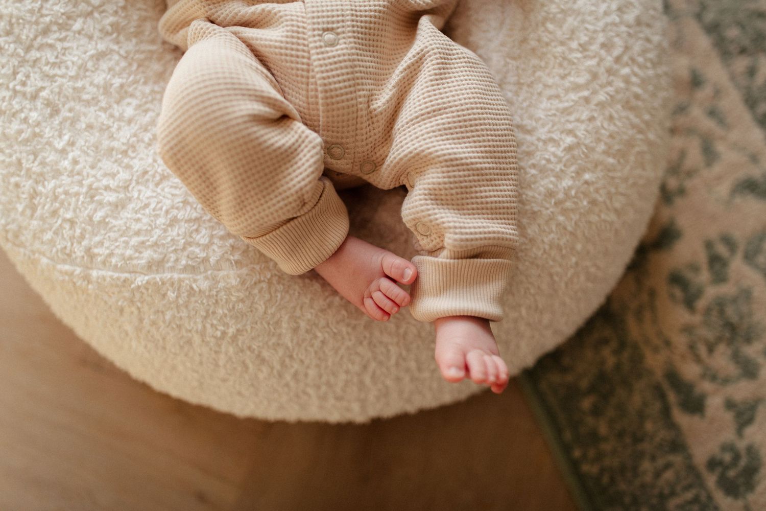 Close-up of baby's feet in beige knit outfit on white cushion.