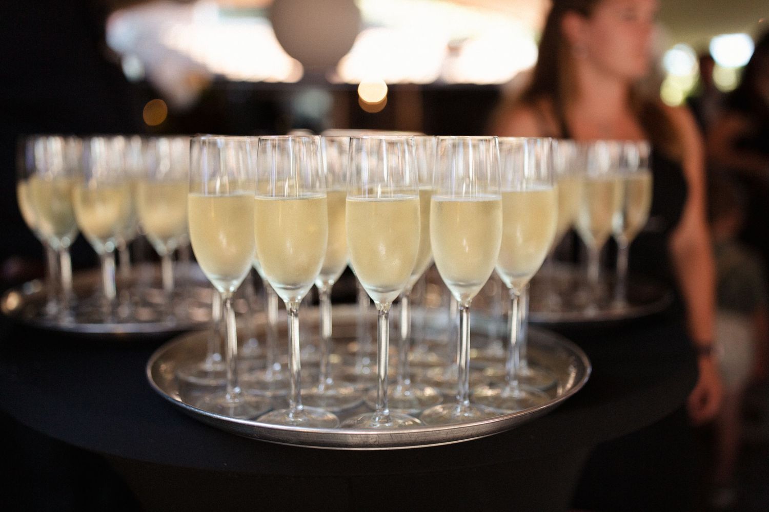 A silver tray holds multiple champagne flutes filled with sparkling wine at an elegant event.
