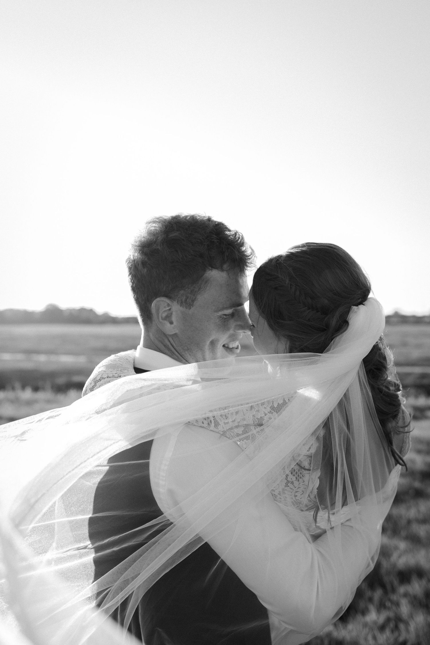 A romantic black and white wedding photograph shows a couple embracing as the bride's veil flows dramatically in the wind.