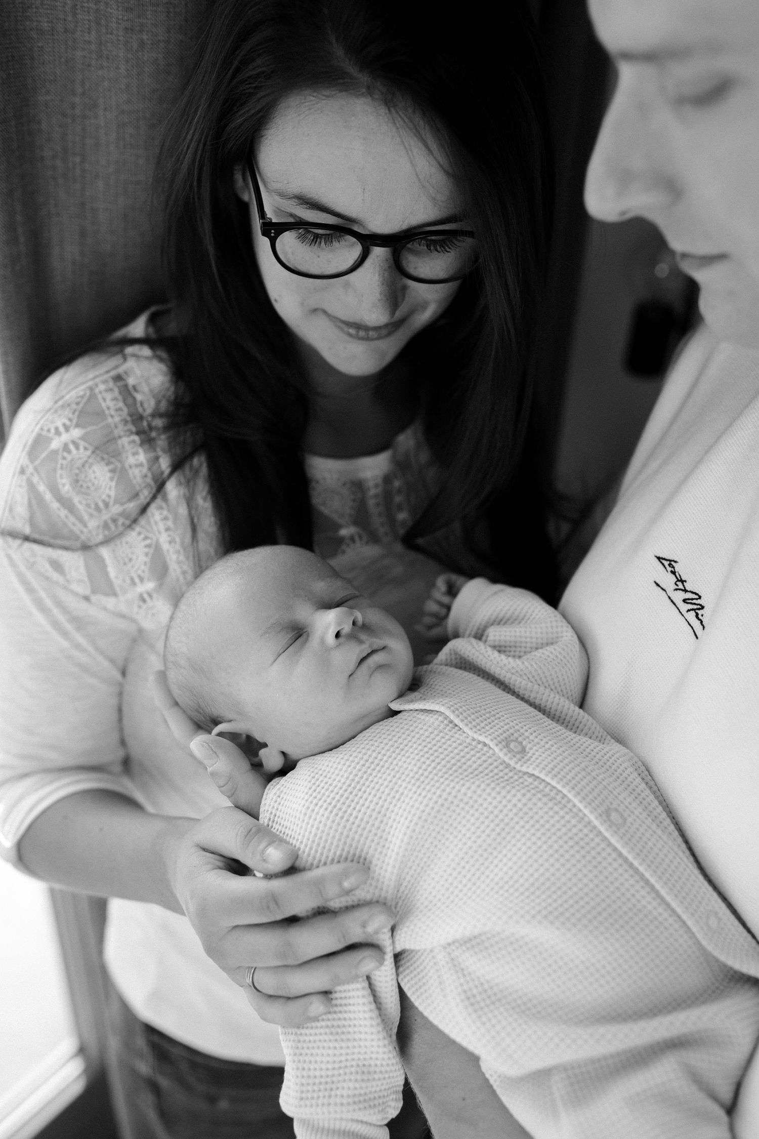 Intimate black and white portrait of sleeping newborn baby being held while wearing a knit onesie.