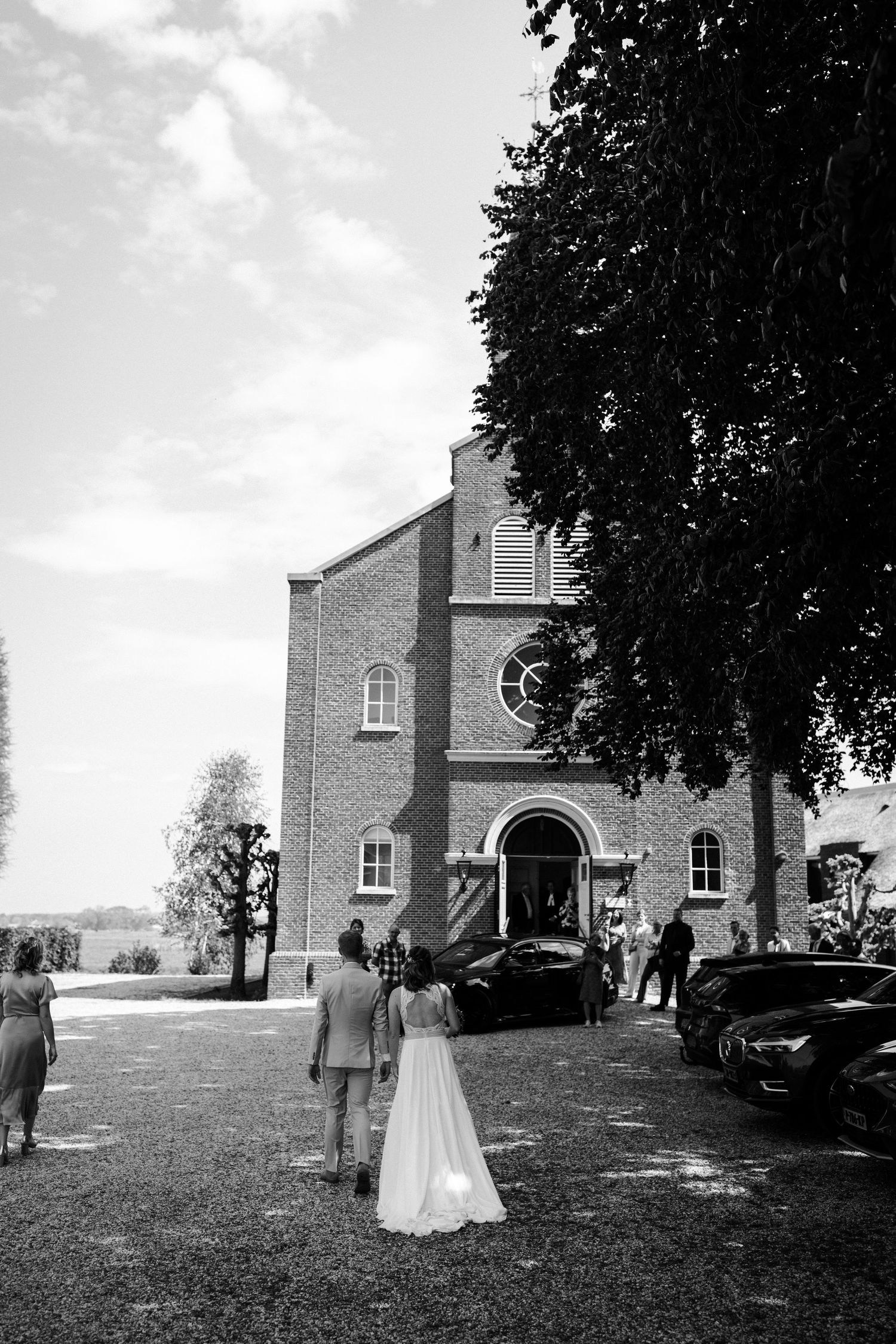 Black and white photo of a couple approaching a brick church entrance.